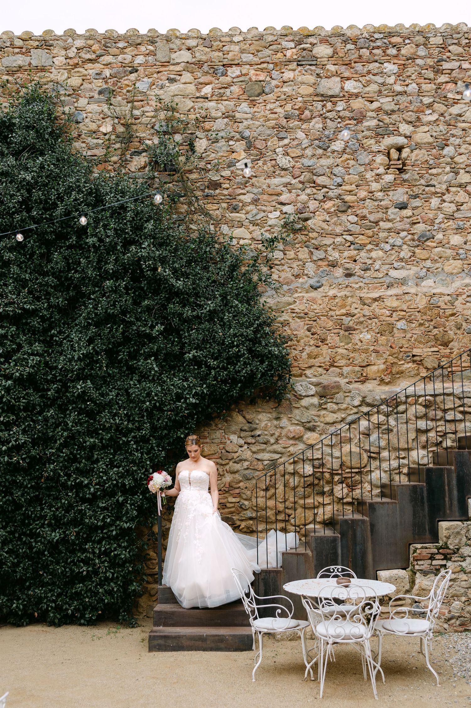 Stone wall courtyard with white garden furniture and lush green landscaping.