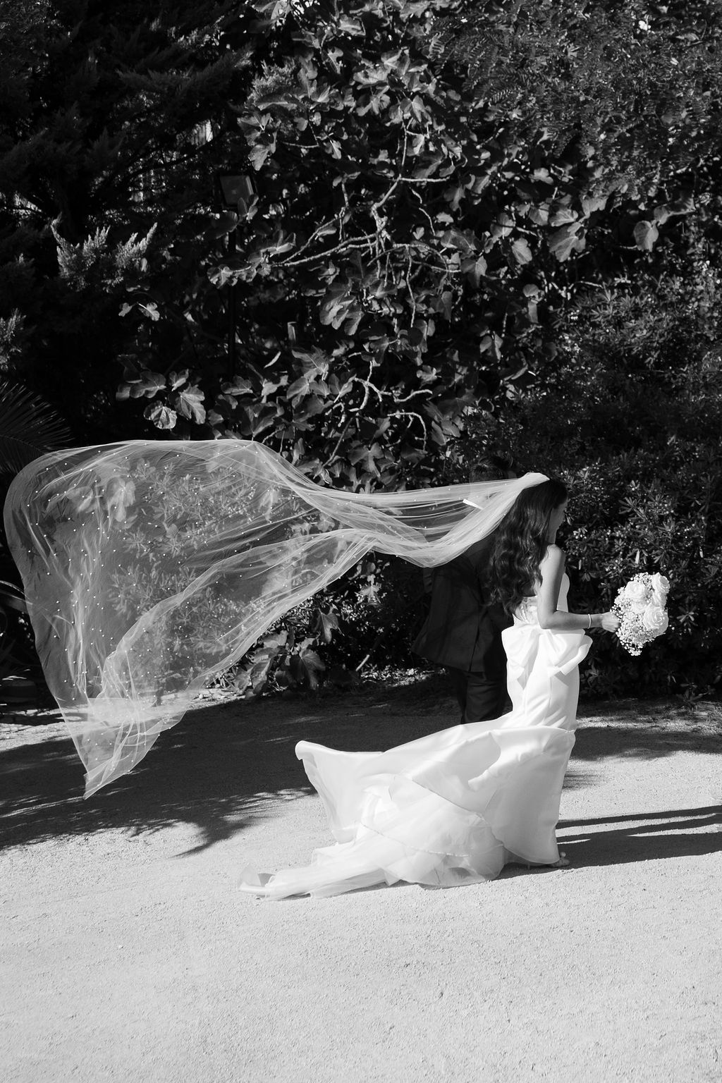 Black and white photo of a bride's veil flowing dramatically in the wind outdoors.