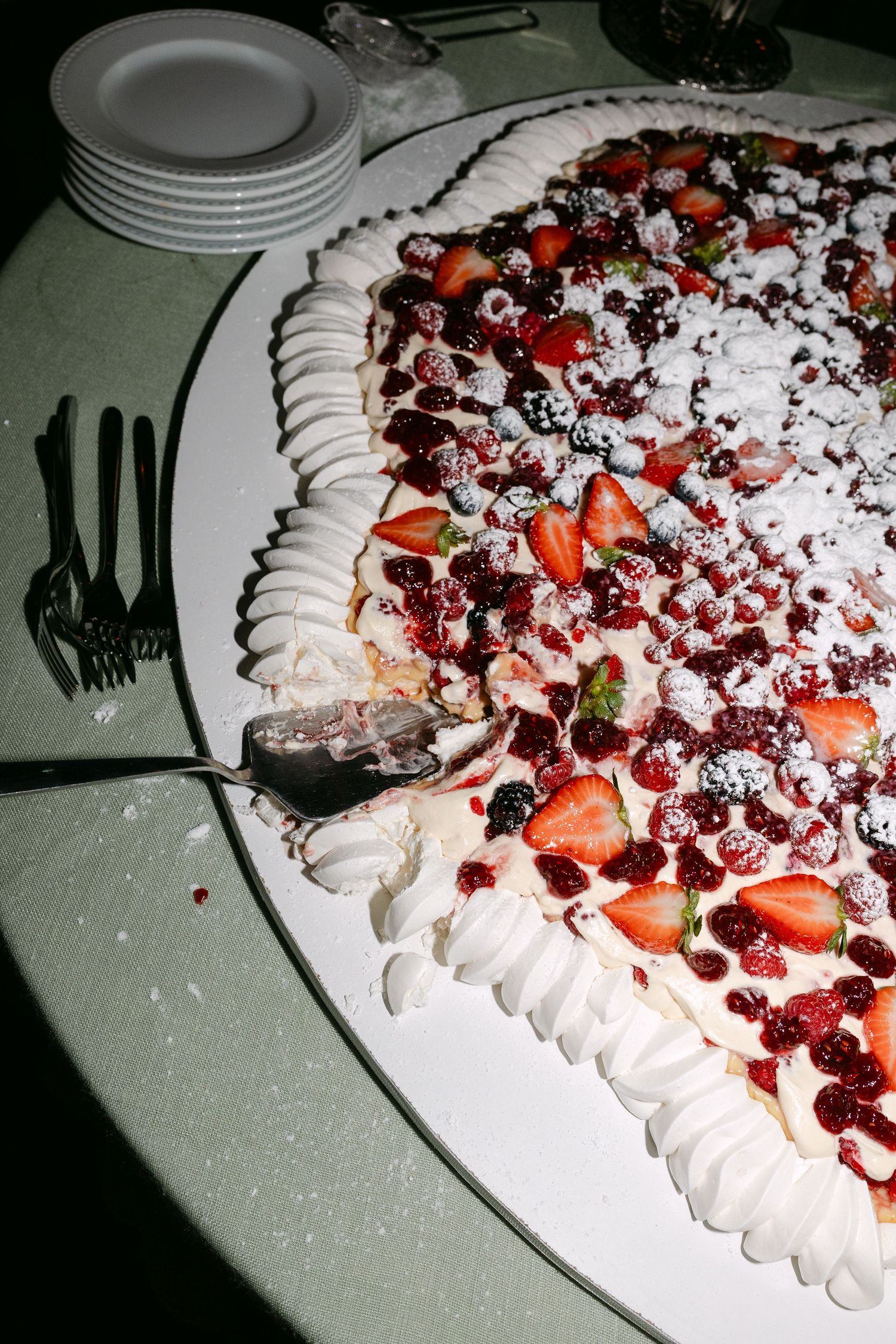 Close-up of an elaborate pavlova dessert topped with fresh berries, cream and powdered sugar.