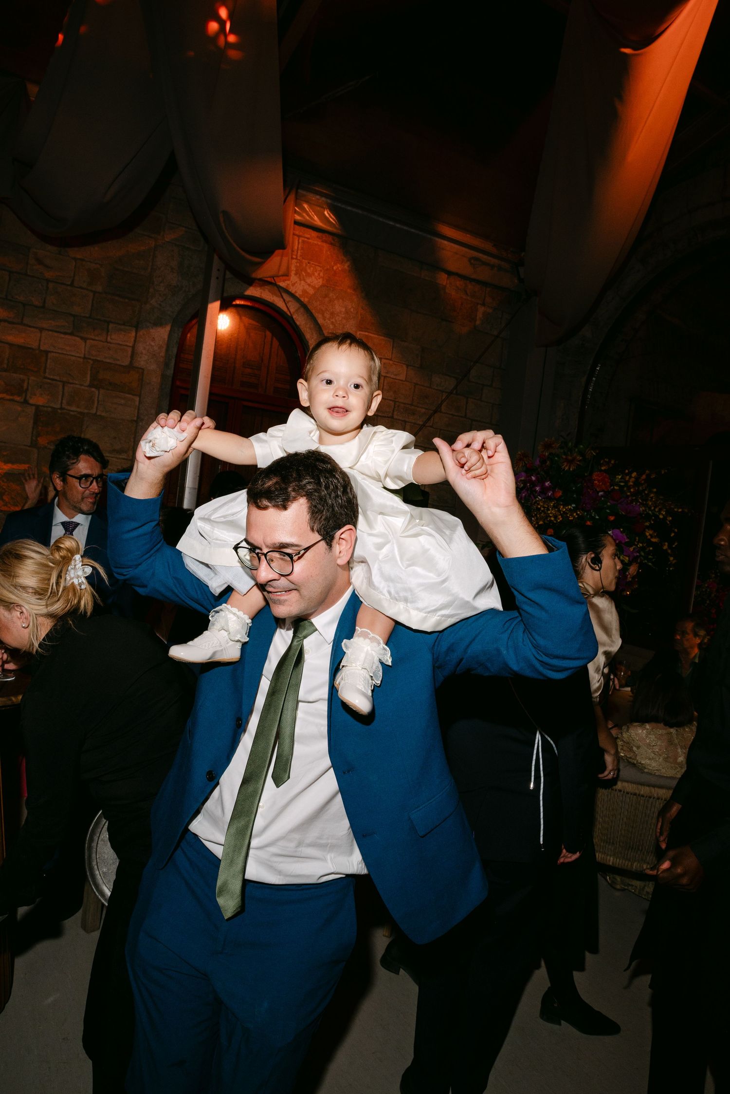 Wedding guests dancing energetically in formal attire under atmospheric lighting.