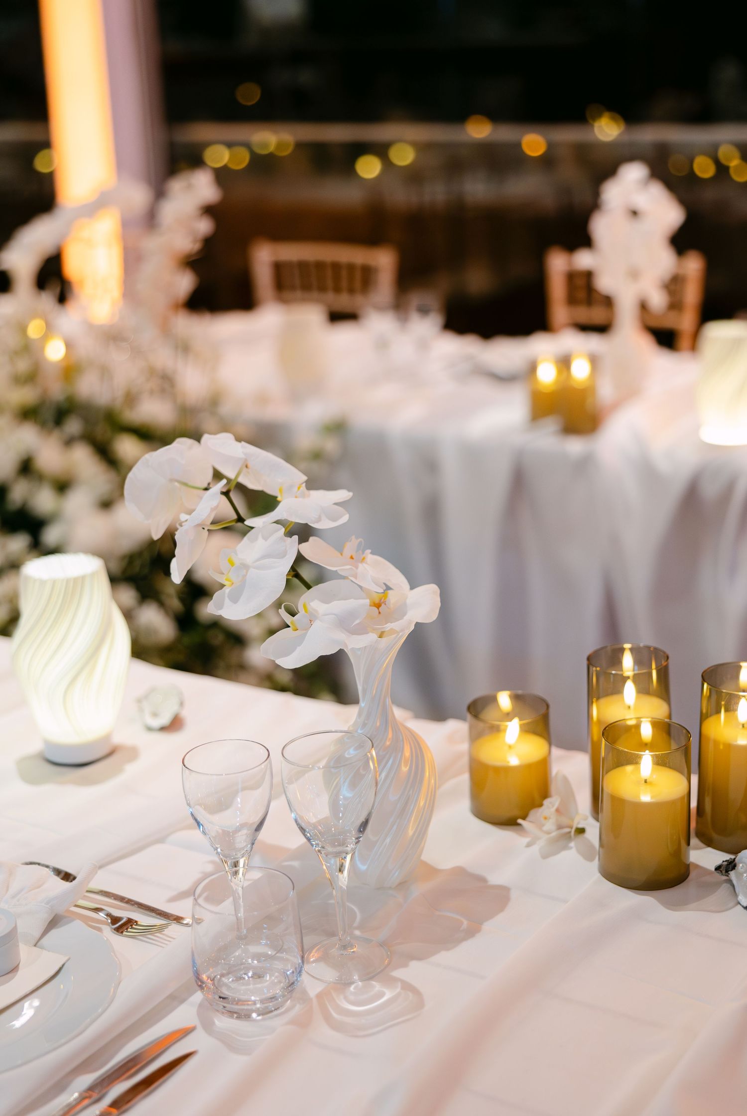Elegant wedding reception table setting with white orchids, candles and glassware.
