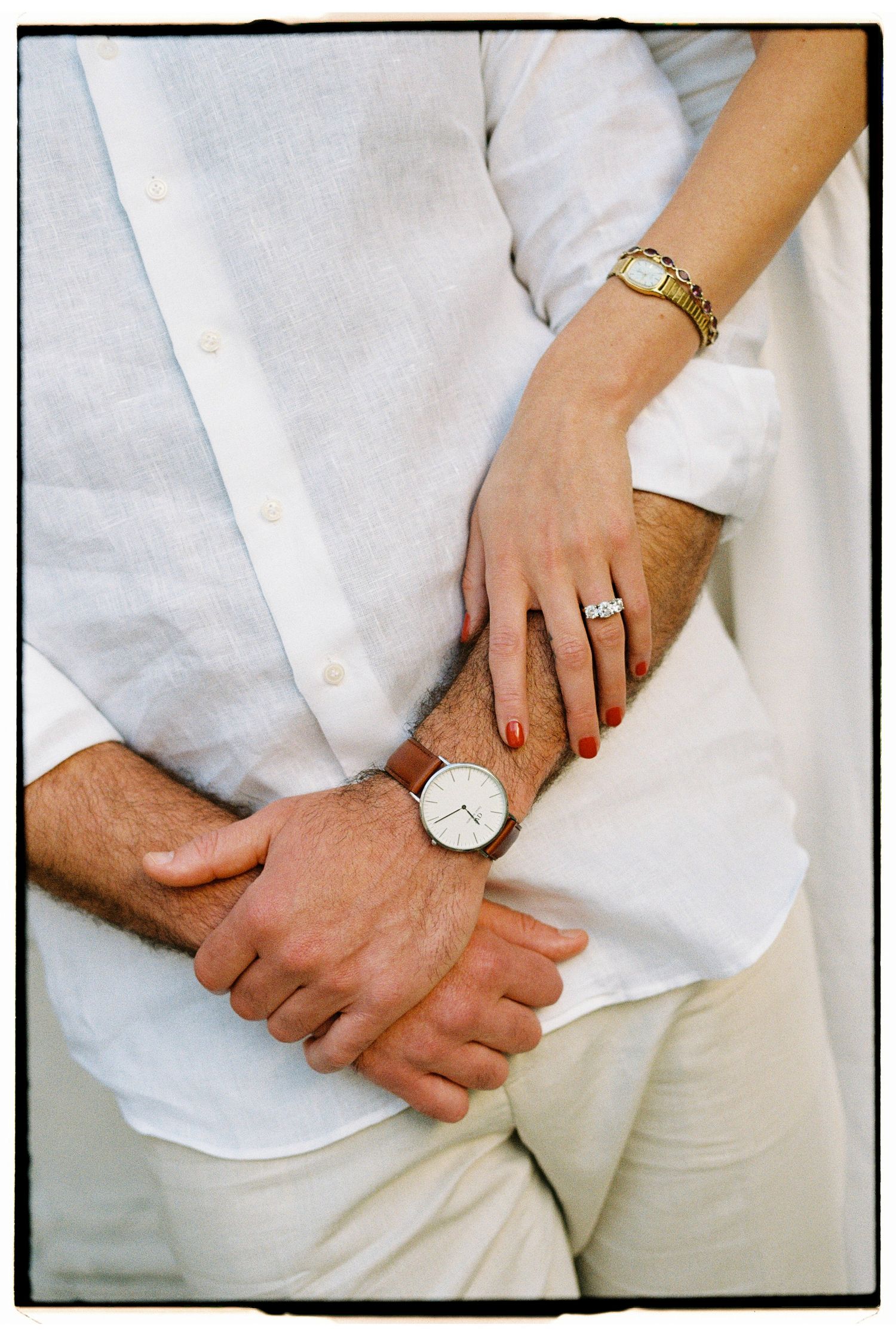 Close-up of couple holding hands, woman wearing diamond ring and gold bracelet, man wearing white watch.