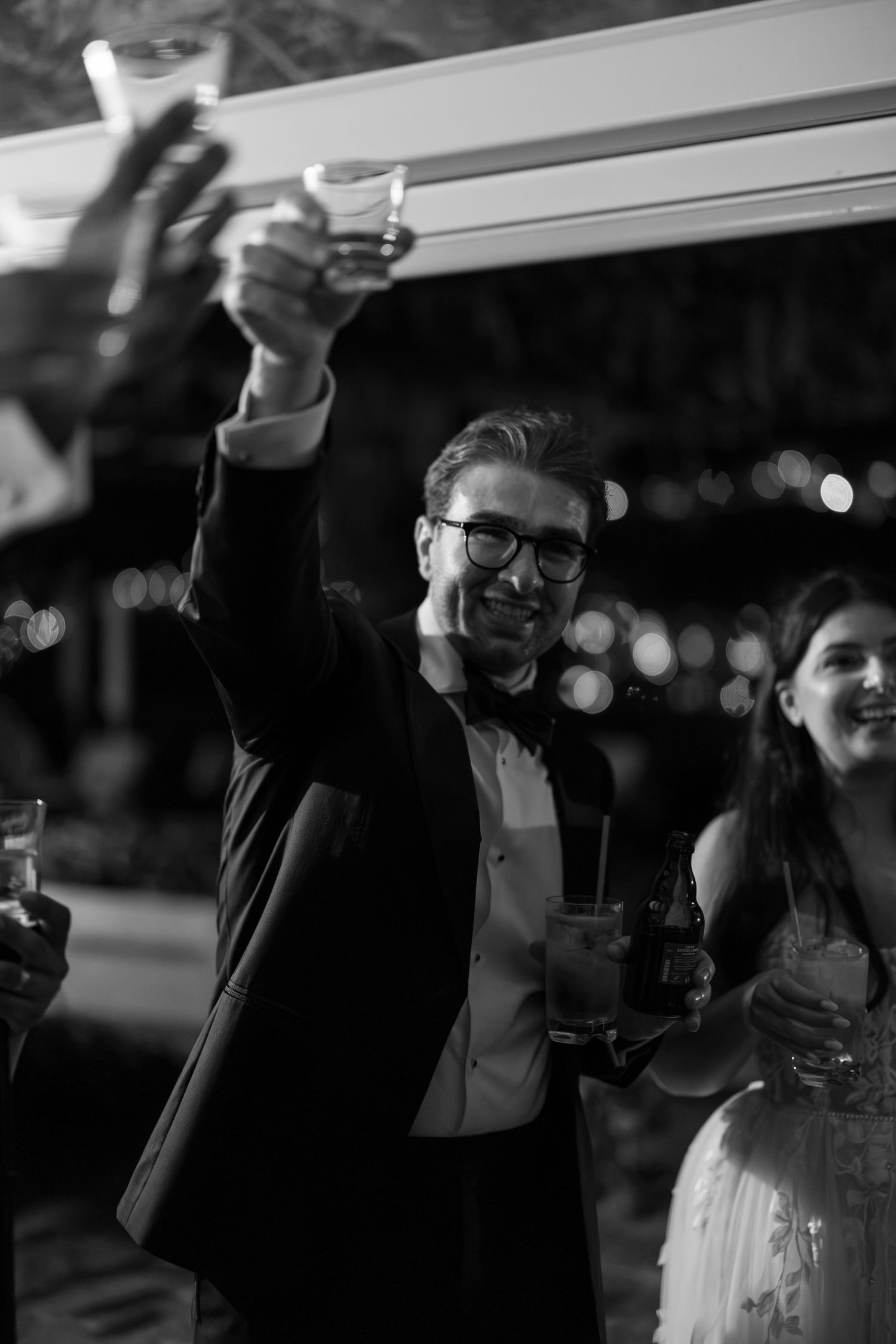 Black and white photo of a smiling man in a tuxedo raising a toast at an elegant evening celebration.