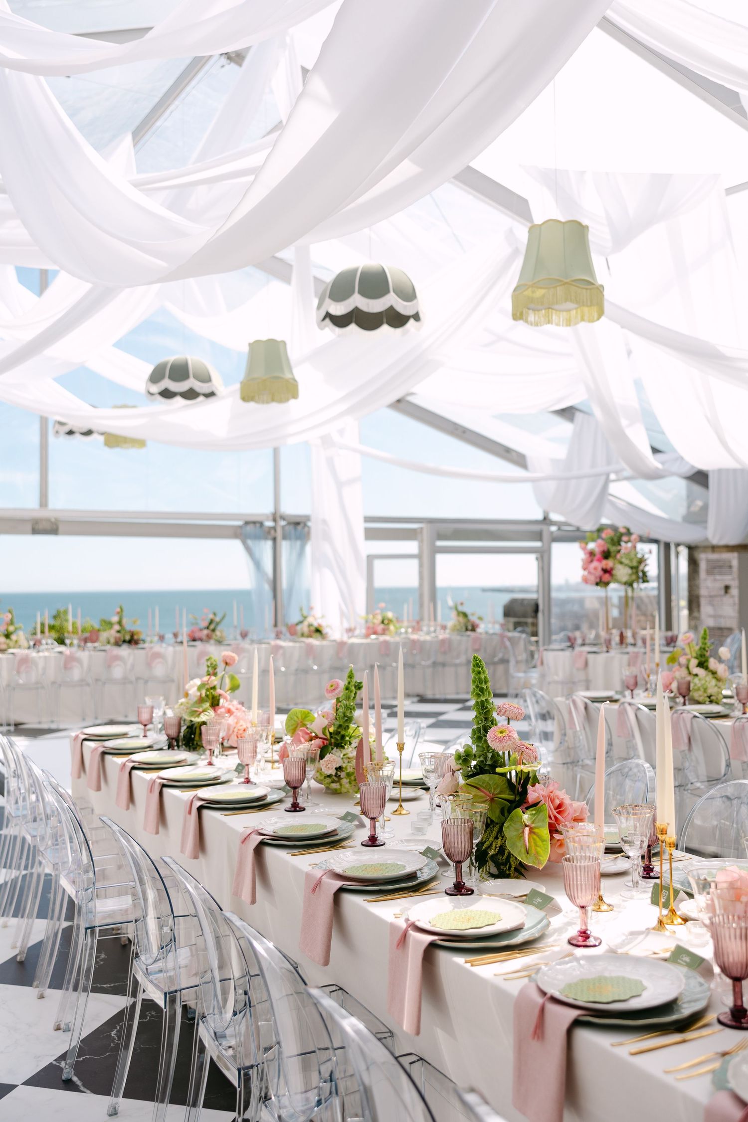 Oceanview wedding reception with white drapes, pink accents, and clear ghost chairs.