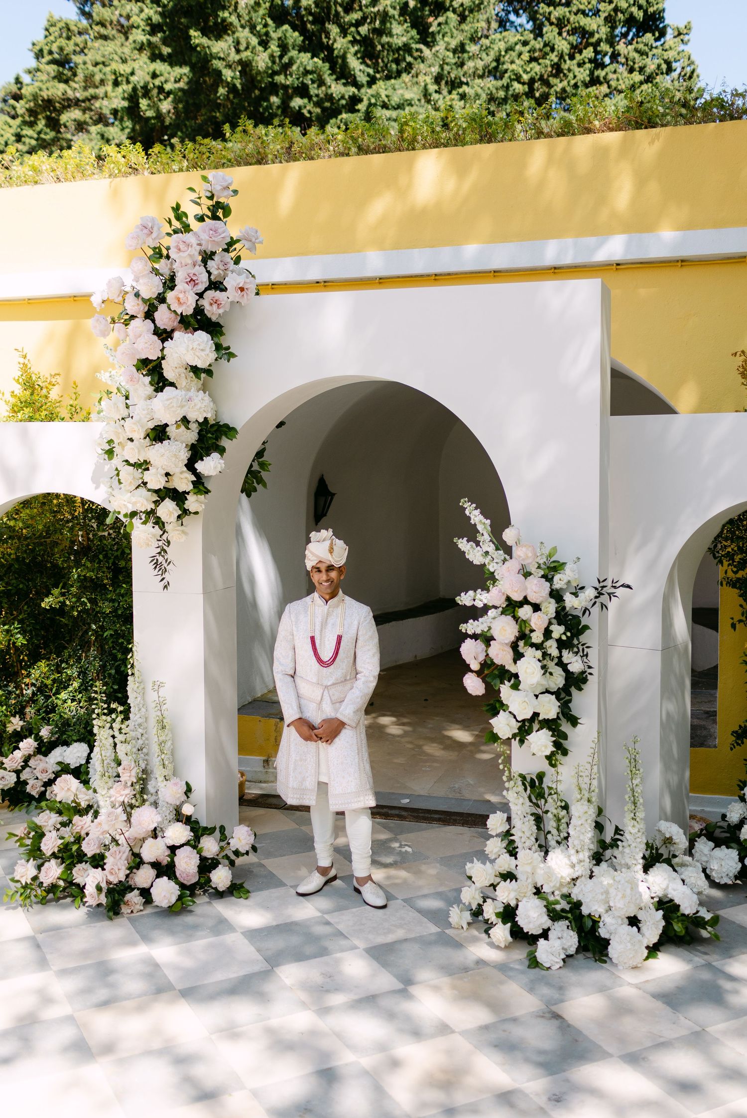 Elegant white floral arch installation with traditional white wedding attire.