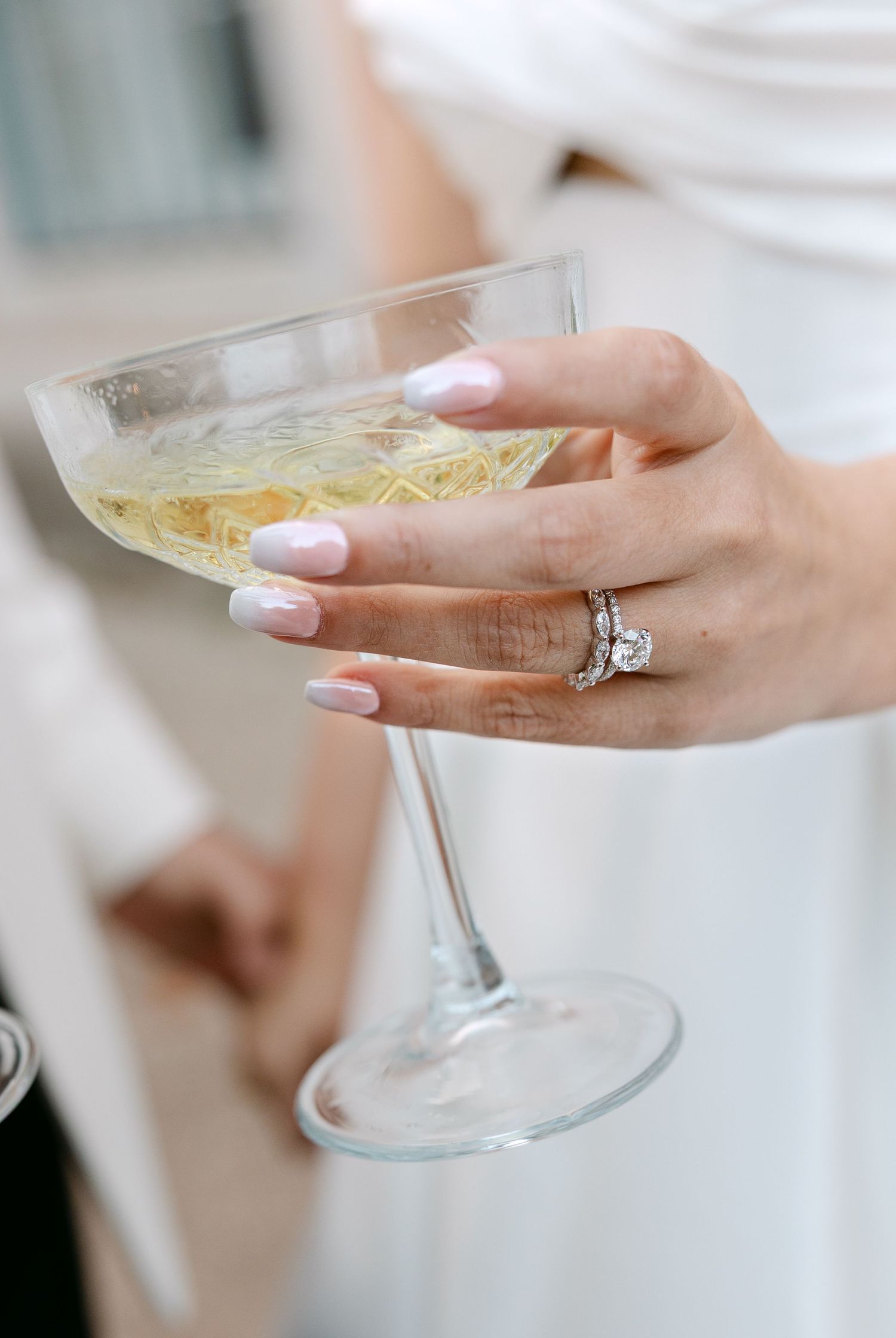Elegant champagne coupe glasses held by hands with manicured nails and sparkling jewelry.