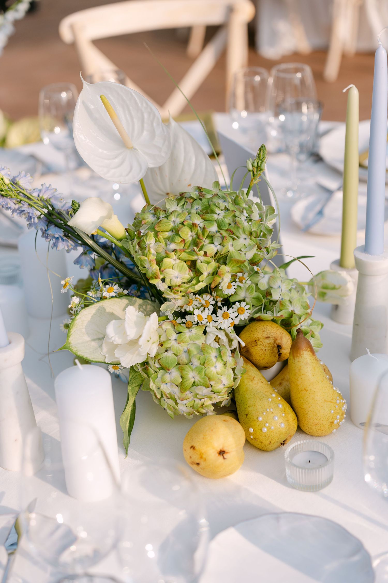 Elegant table centerpiece with white flowers, greenery and fresh pears on a white tablecloth.