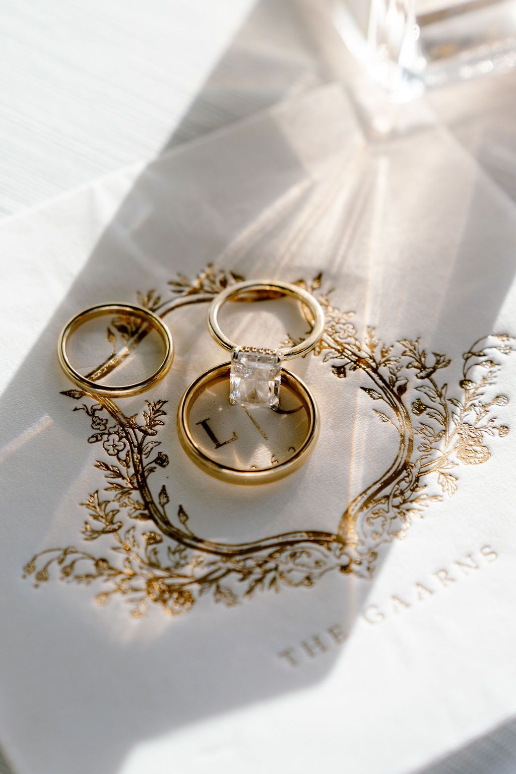 Three gold wedding rings arranged on decorative paper with elegant golden floral designs.