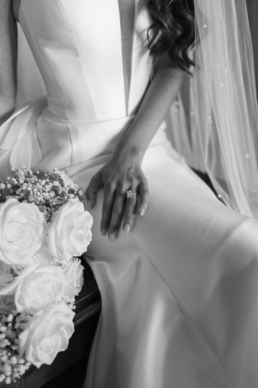 Black and white detail shot of a bride's wedding dress, bouquet, and engagement ring.