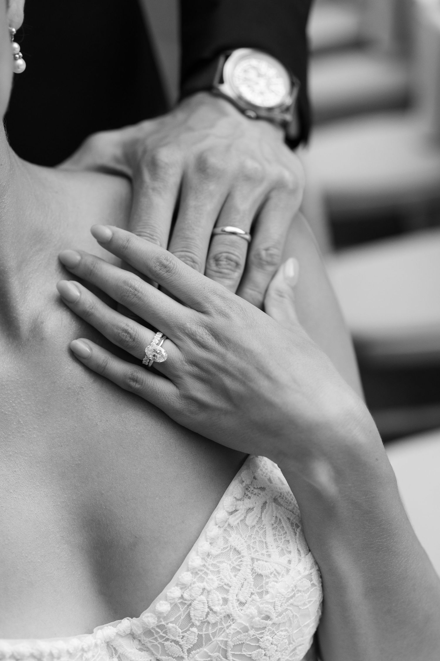 Close-up black and white photo of wedding rings and lace dress detail.