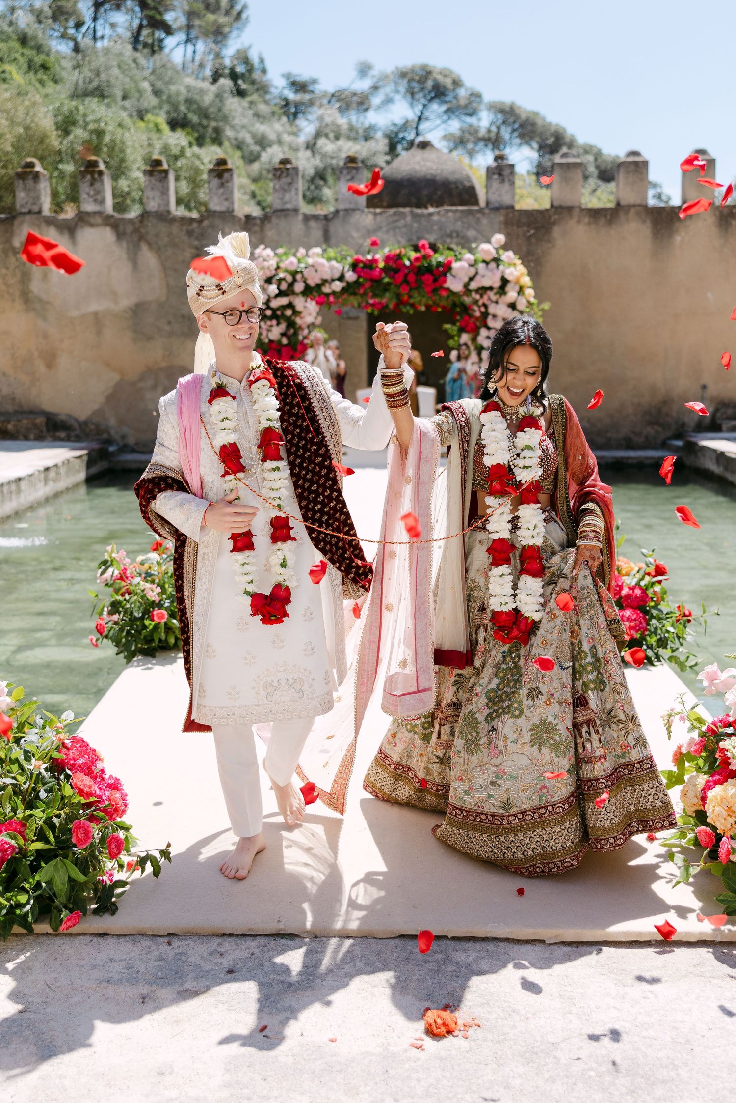 Wedding ceremony captured in sequence with red rose petals falling against stone courtyard backdrop.