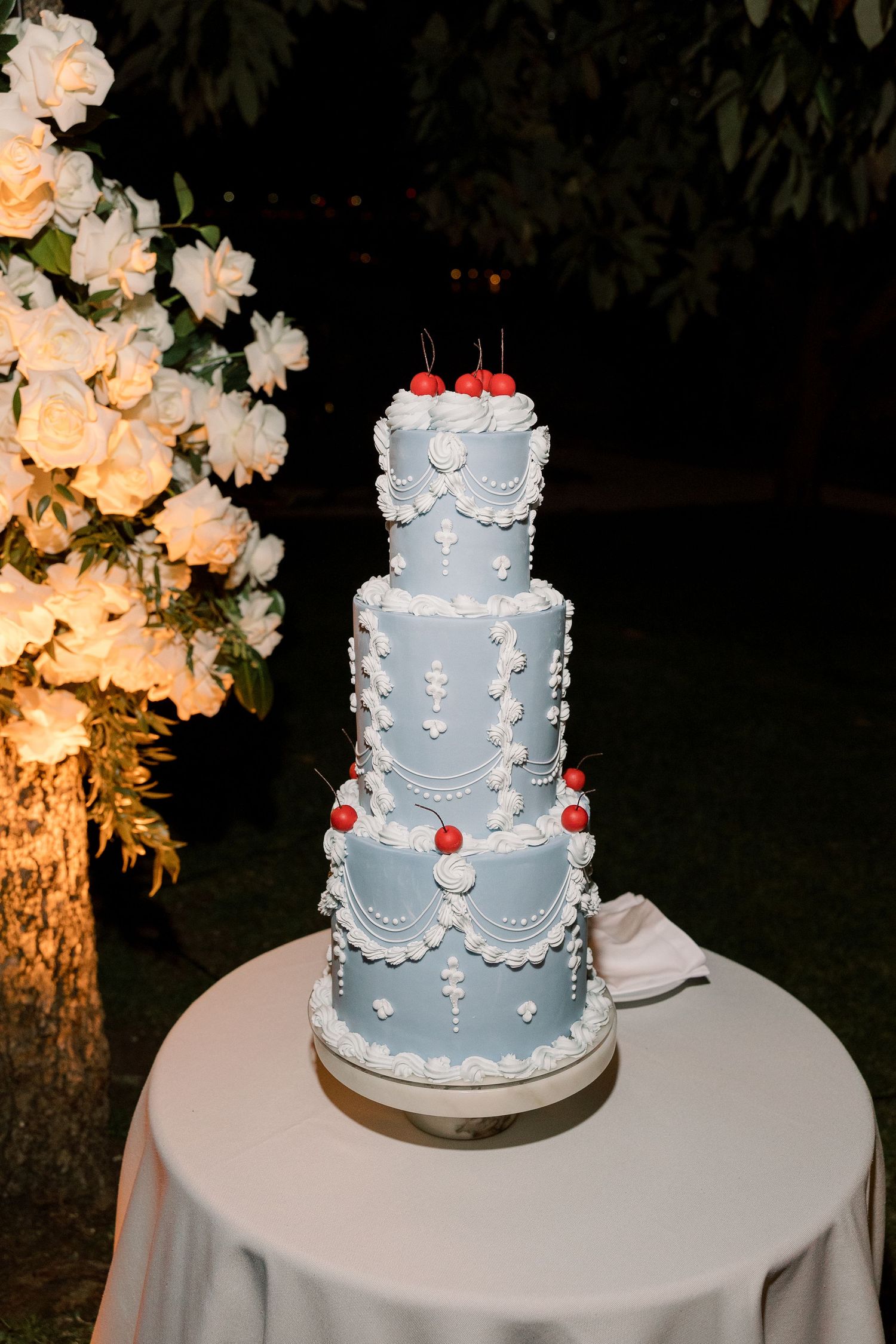 Elegant three-tier light blue wedding cake decorated with white details and red accents.