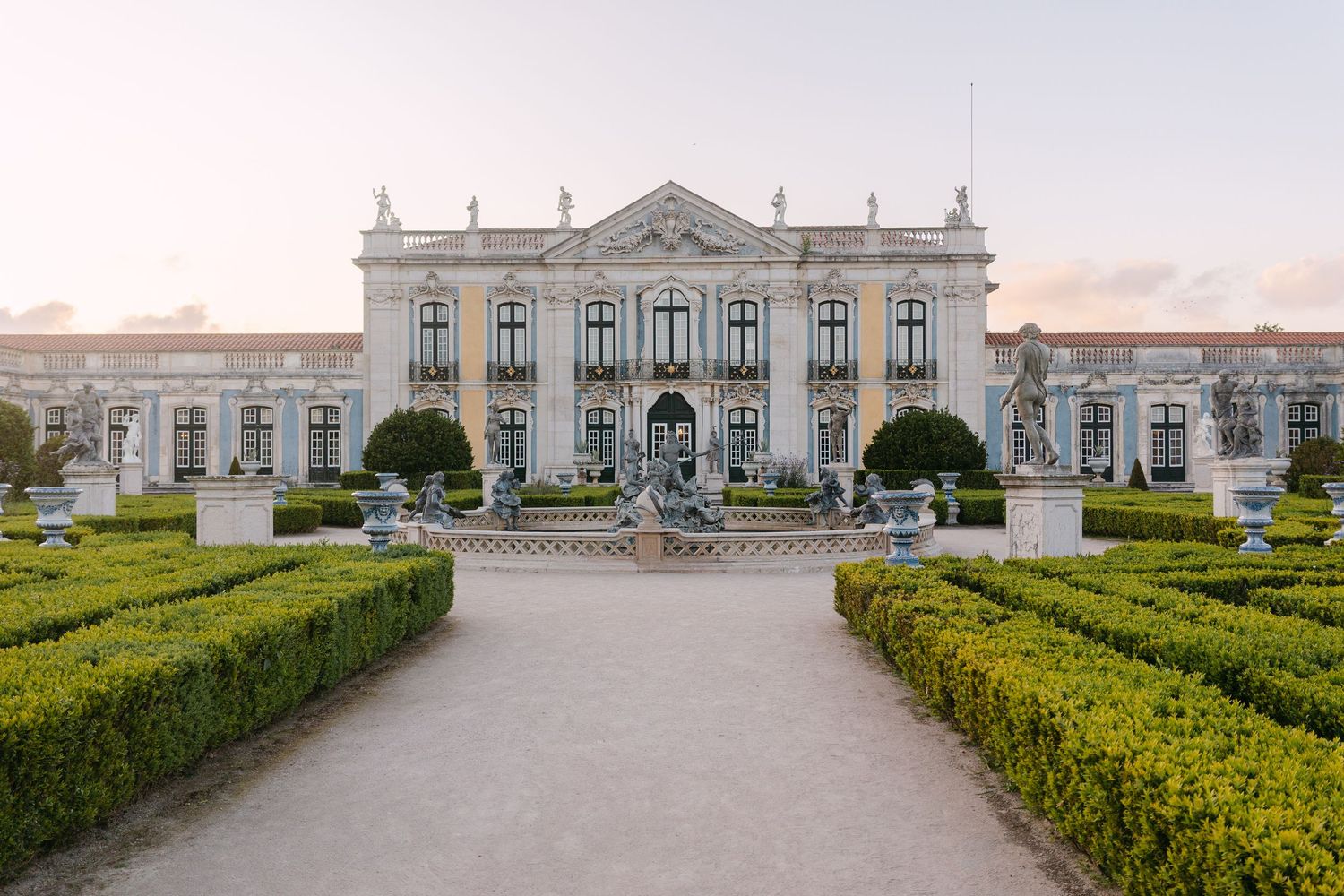 Symmetrical view of elegant white palace with manicured gardens and hedges.
