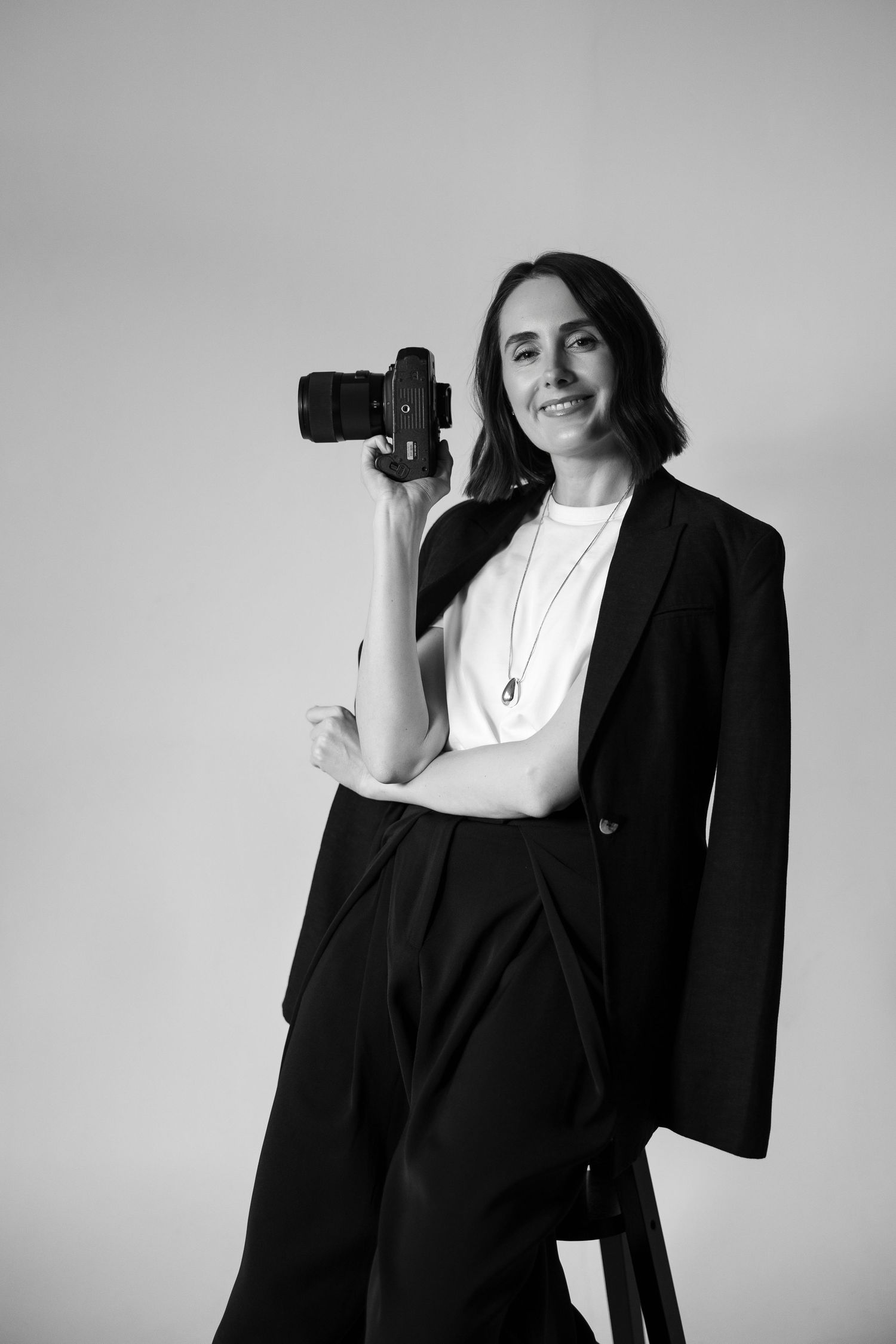 Fashion photoshoot series showing model in black blazer and white top against grey backdrop.