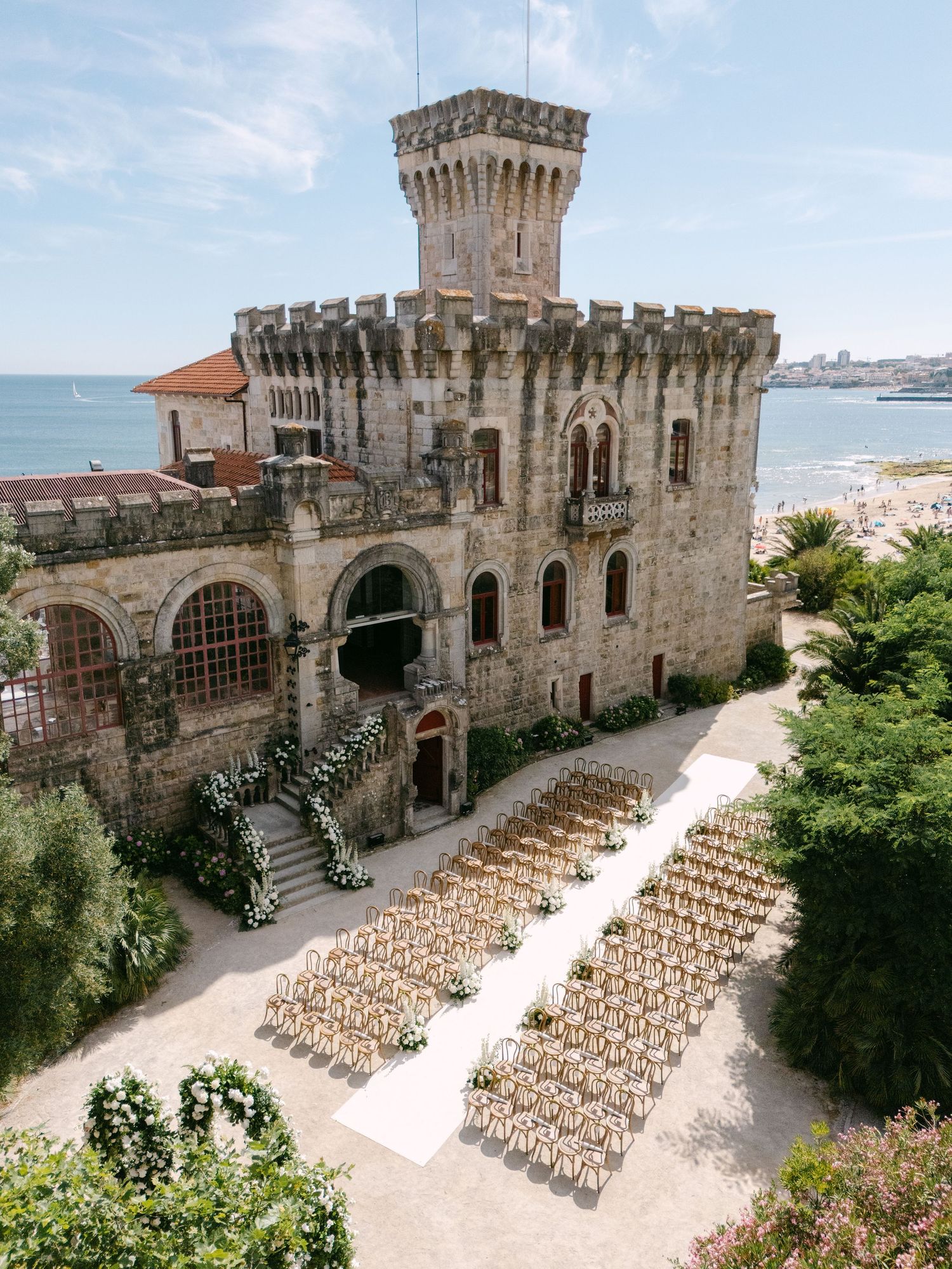 Stone castle venue with rows of wooden chairs set up for an outdoor wedding ceremony by the sea.
