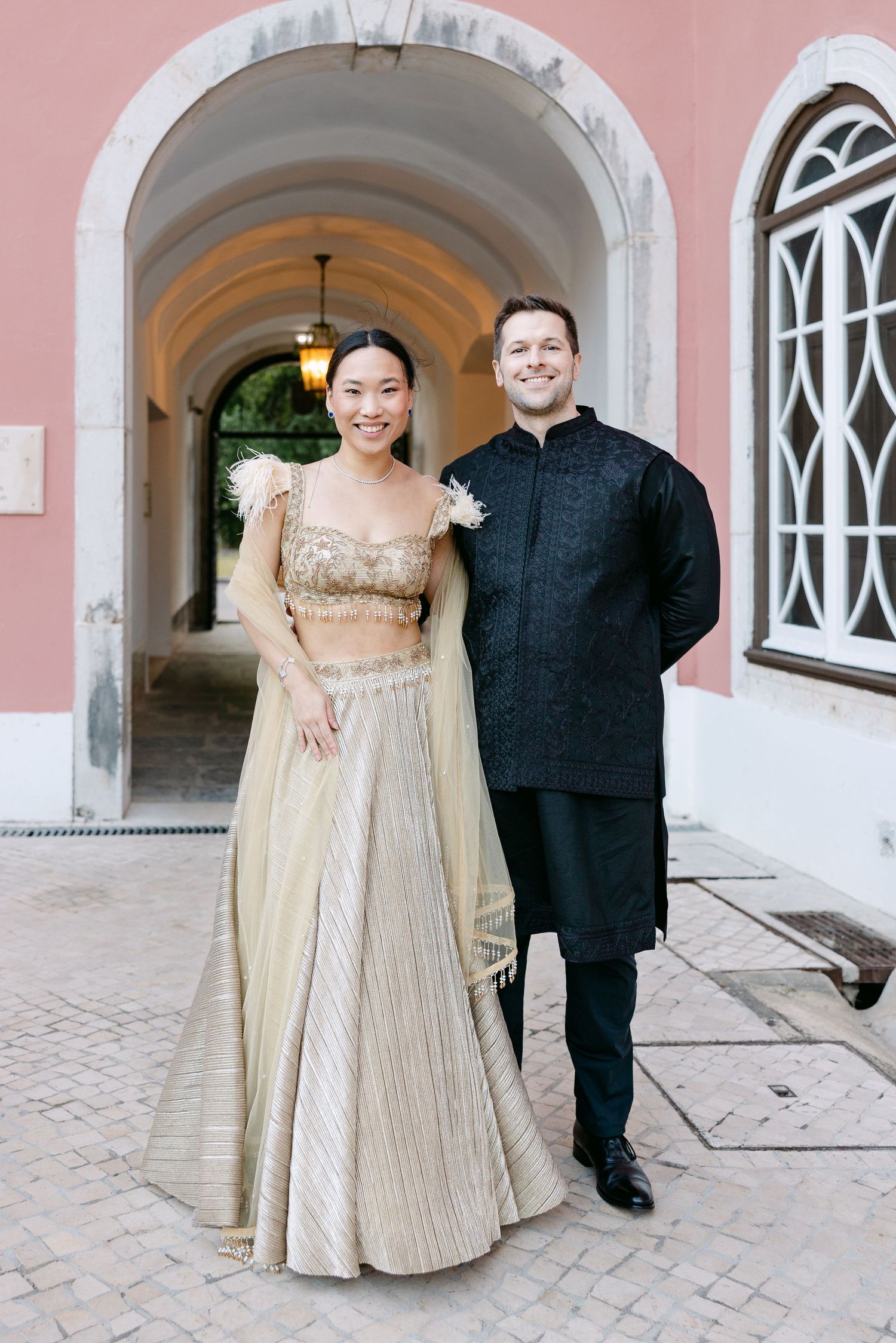 A couple poses under an archway in fusion wedding attire.