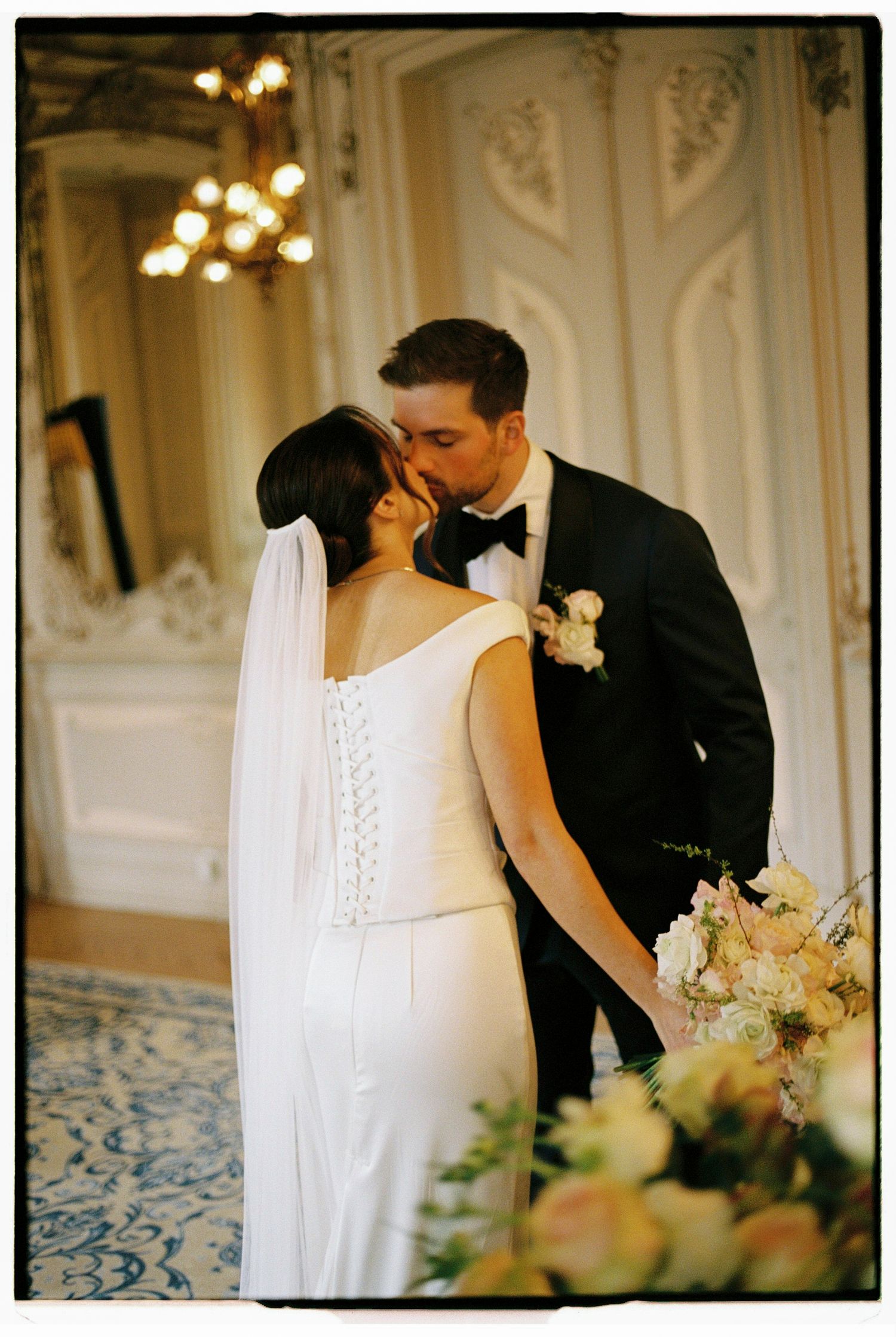 Bride and groom sharing a first kiss at the altar, with the bride holding a pastel bouquet in an ornate venue.