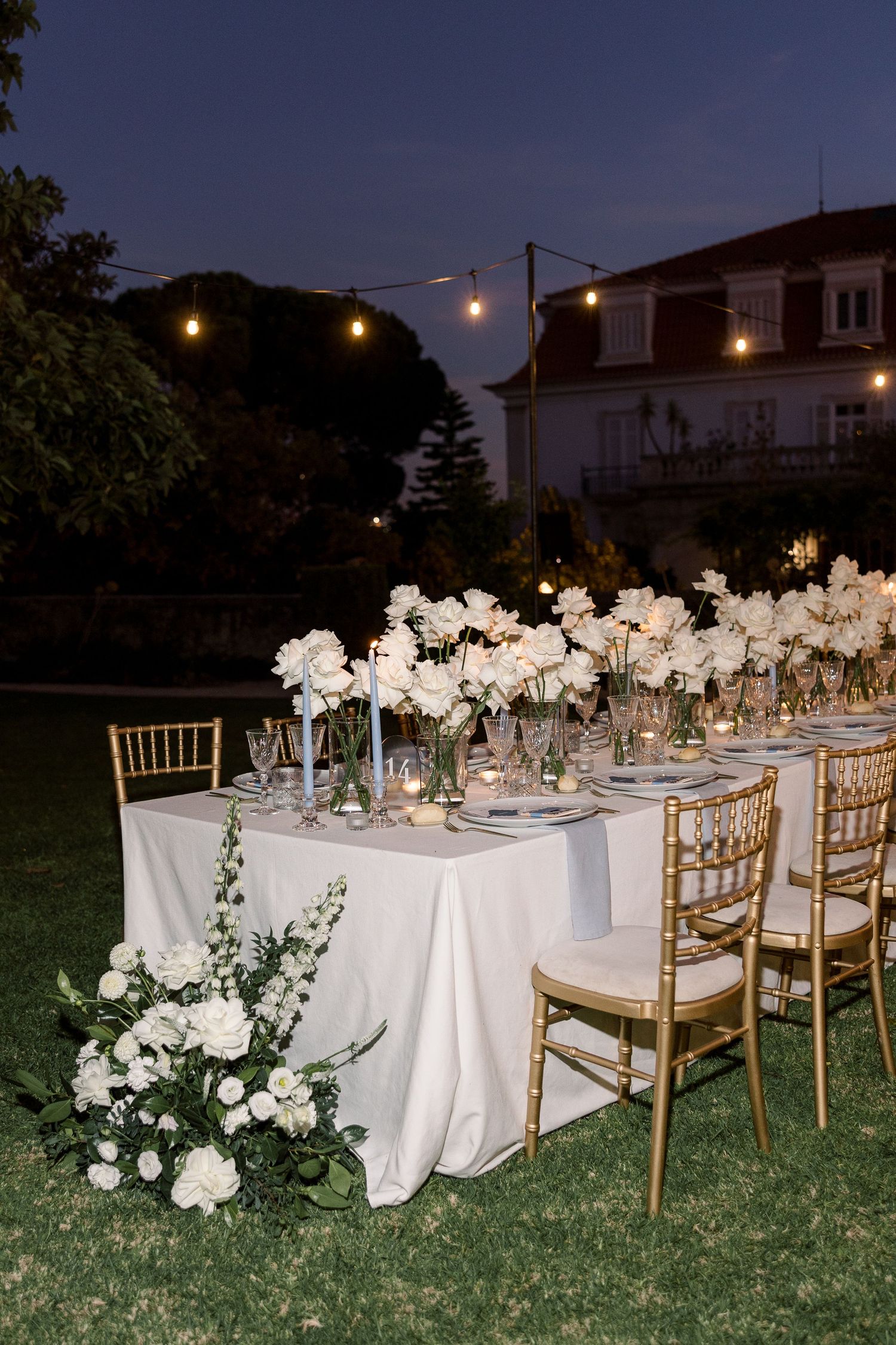 Outdoor wedding reception tables set with white linens and floral centerpieces at dusk.