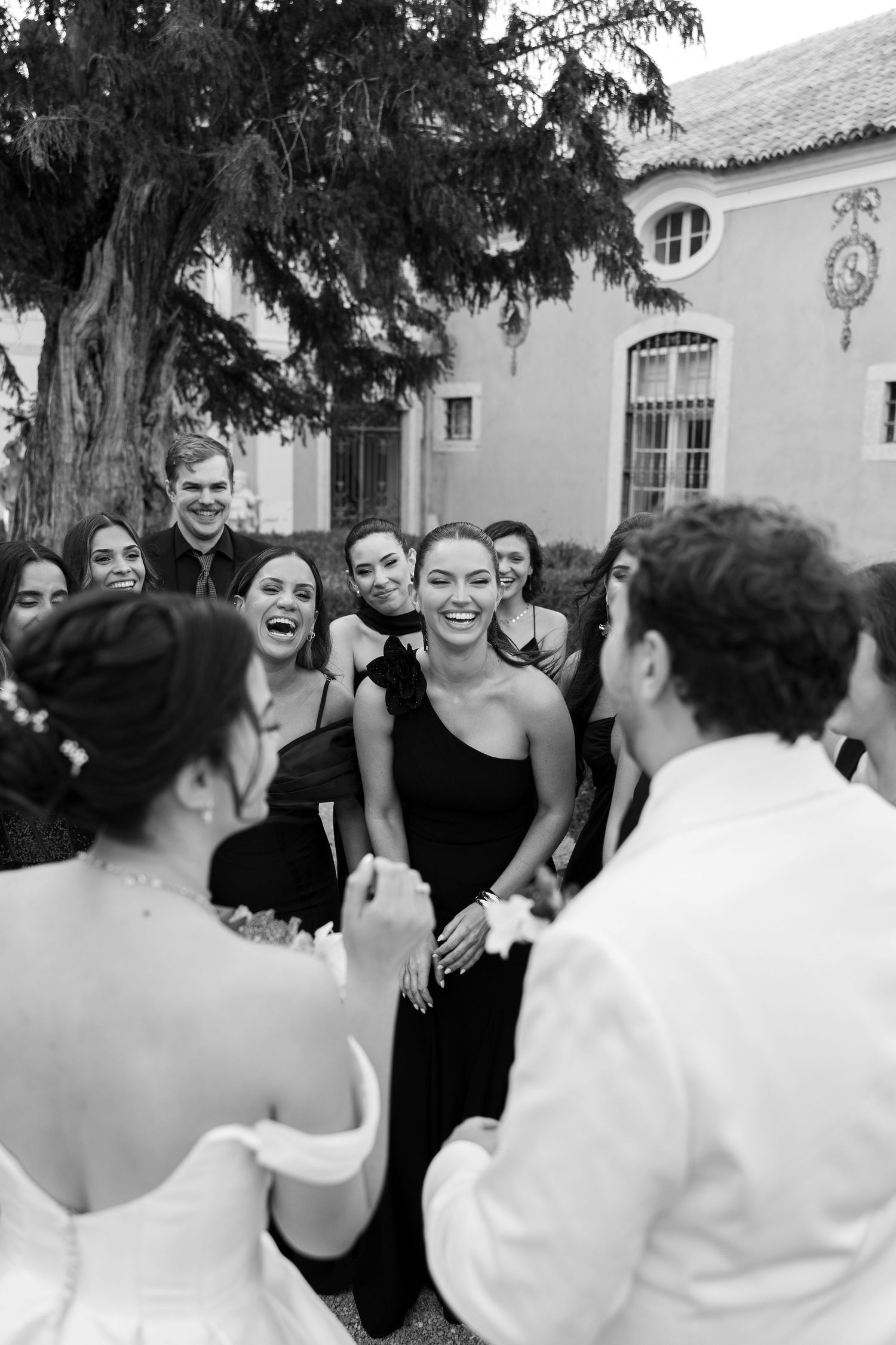 Wedding party shares joyful laughter and candid moments in black and white photography.