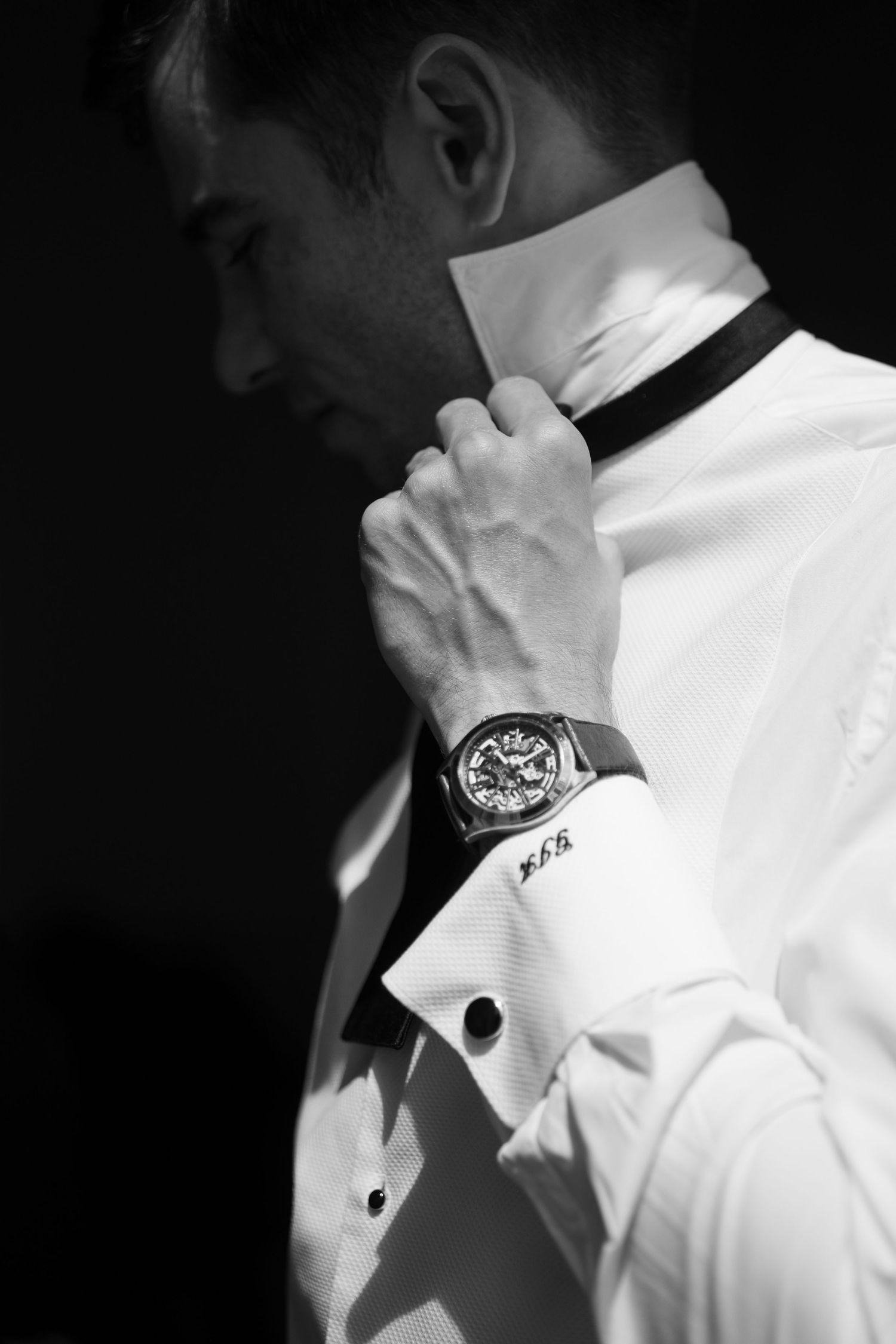 Elegant white dress shirt with cufflinks and watch details shown in dramatic lighting.