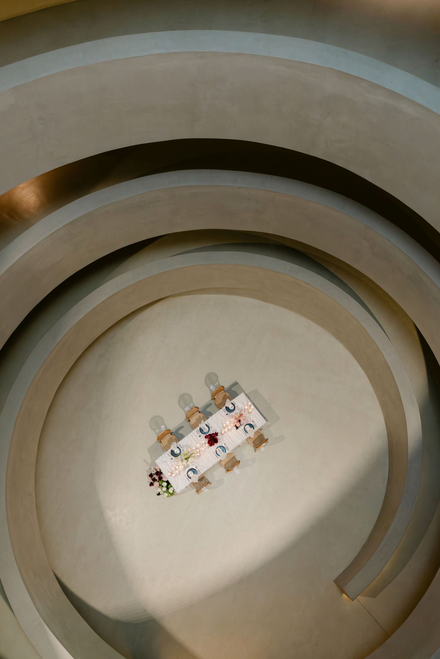 Aerial view of a small dining table set for a meal, centered within concentric circular architectural curves.