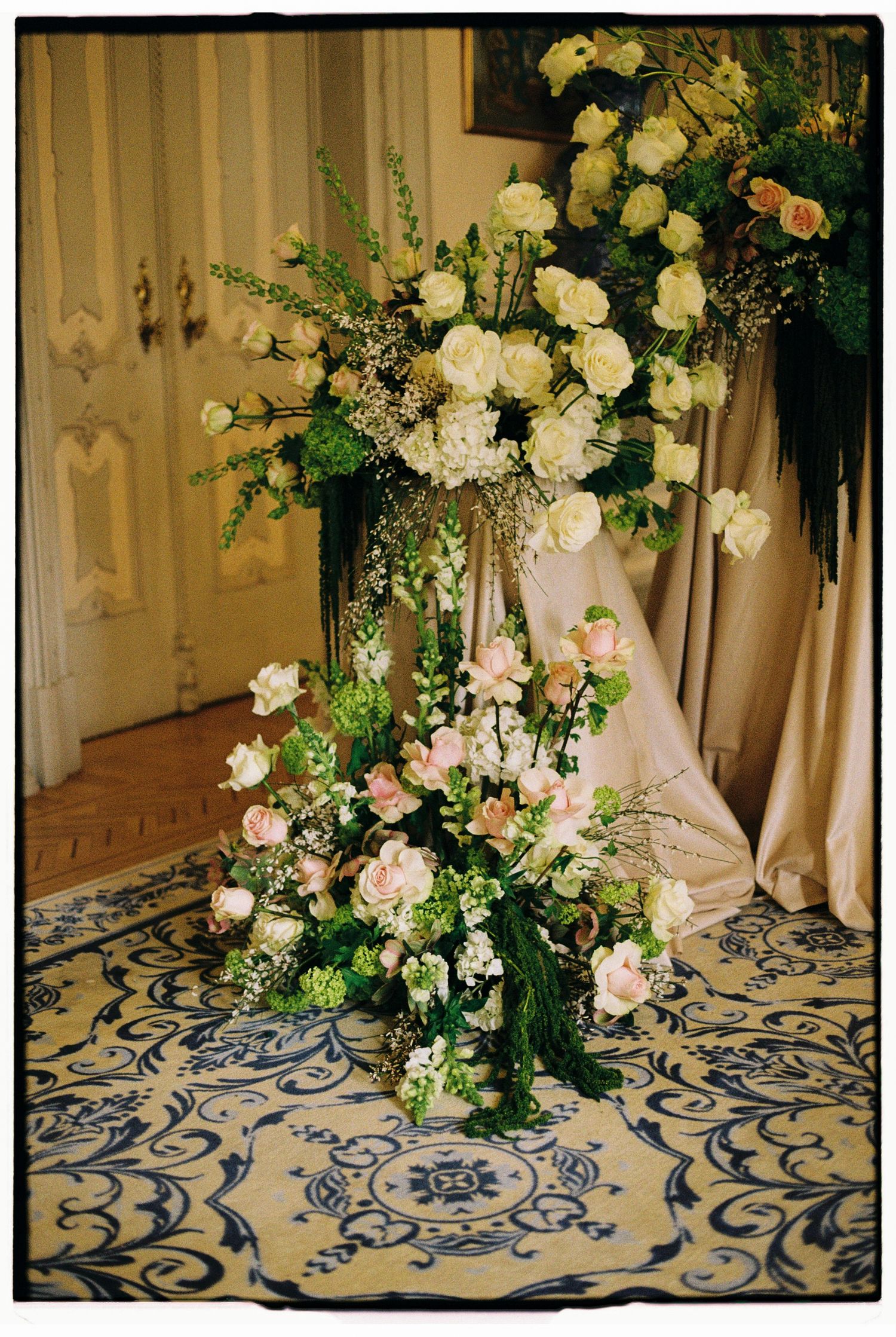 Elegant floral arrangement with white and pink roses, greenery on ornate stand, perfect for weddings or formal events.