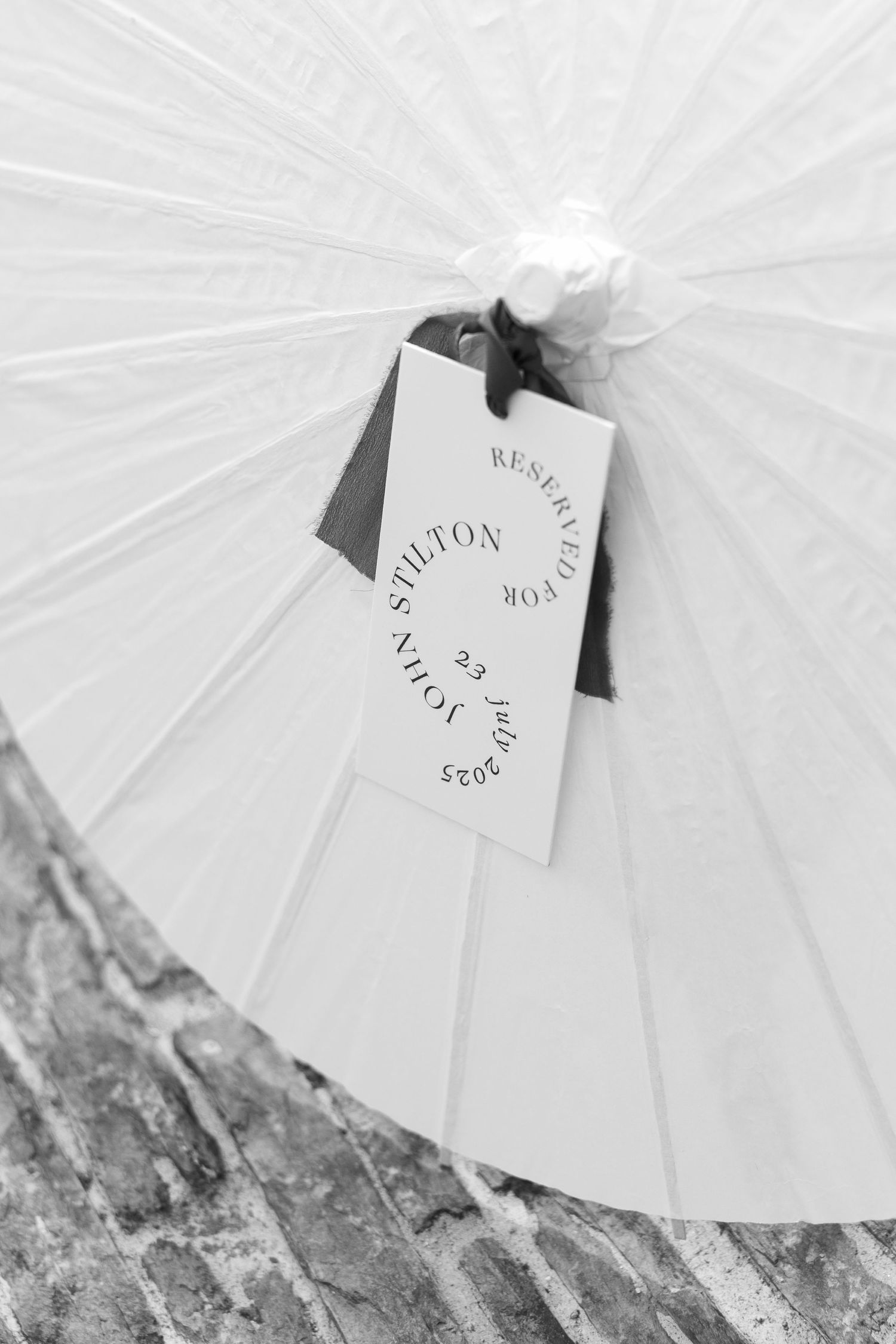 Close-up of a white parasol with a circular wedding tag reading Reserved for Stilton, John S.