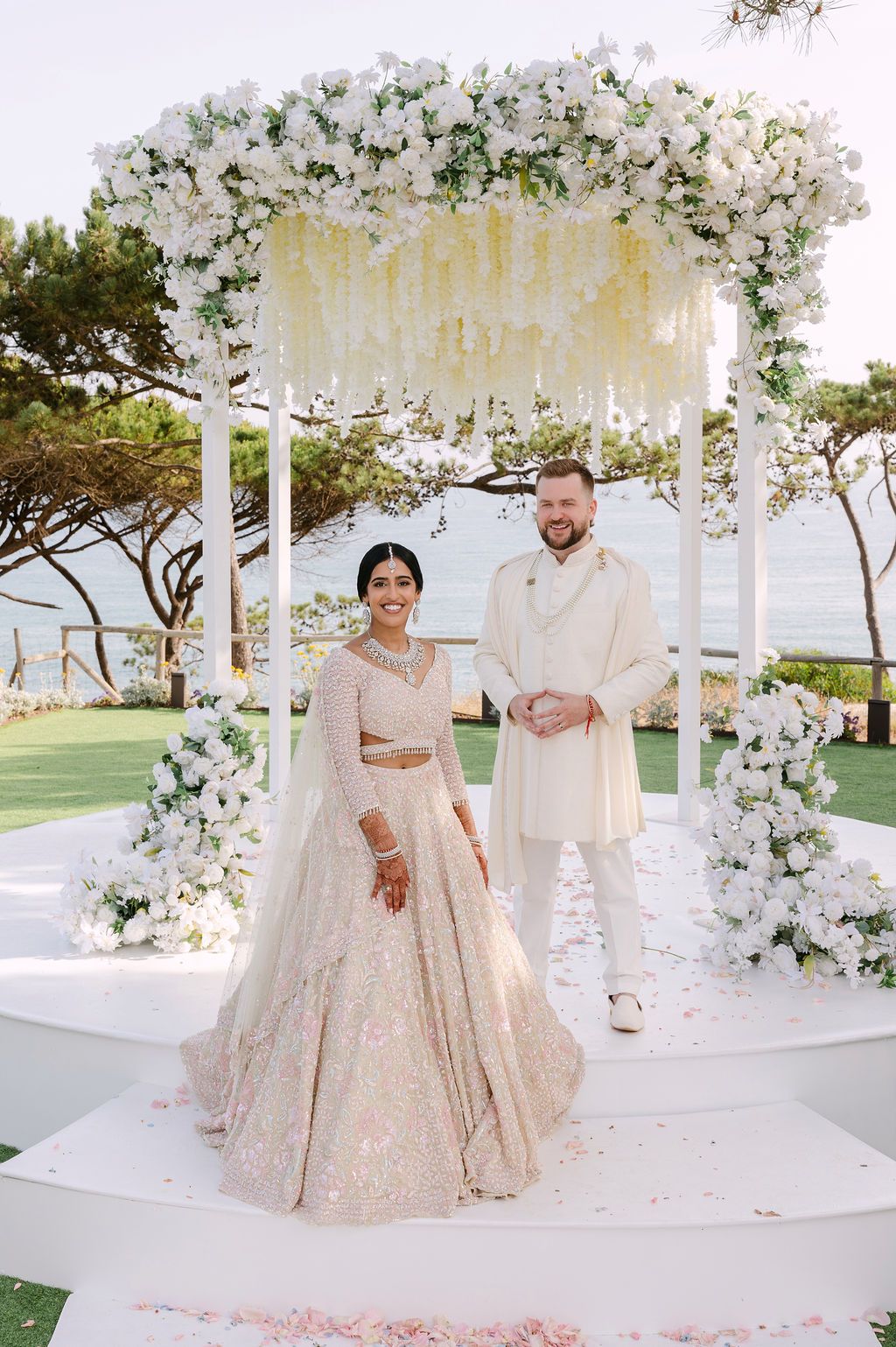 Elegant white floral mandap decorated with roses and draped fabric for an outdoor wedding ceremony.