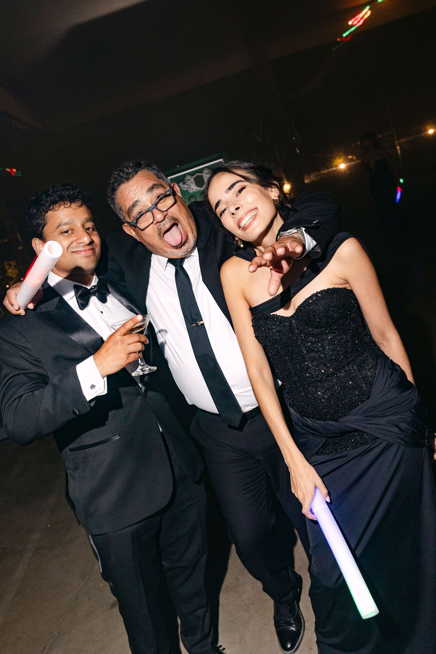Three elegantly dressed guests in formal attire pose playfully at an evening celebration.