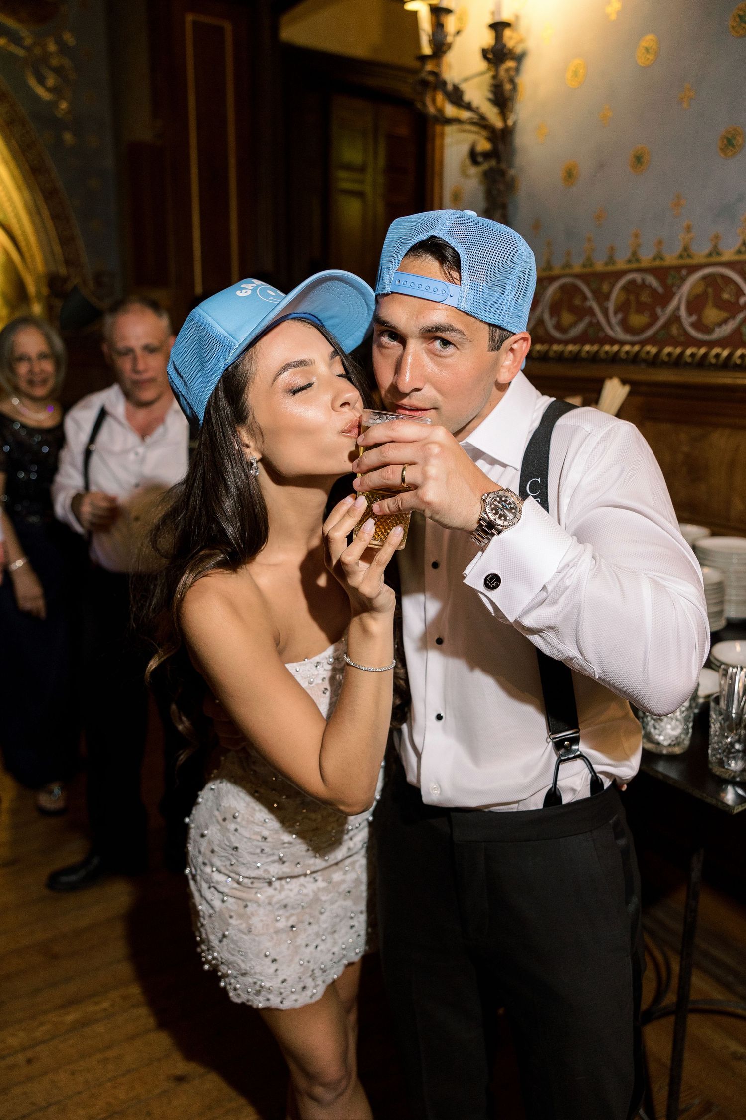 Couple in matching light blue caps sharing a celebratory moment at their reception.