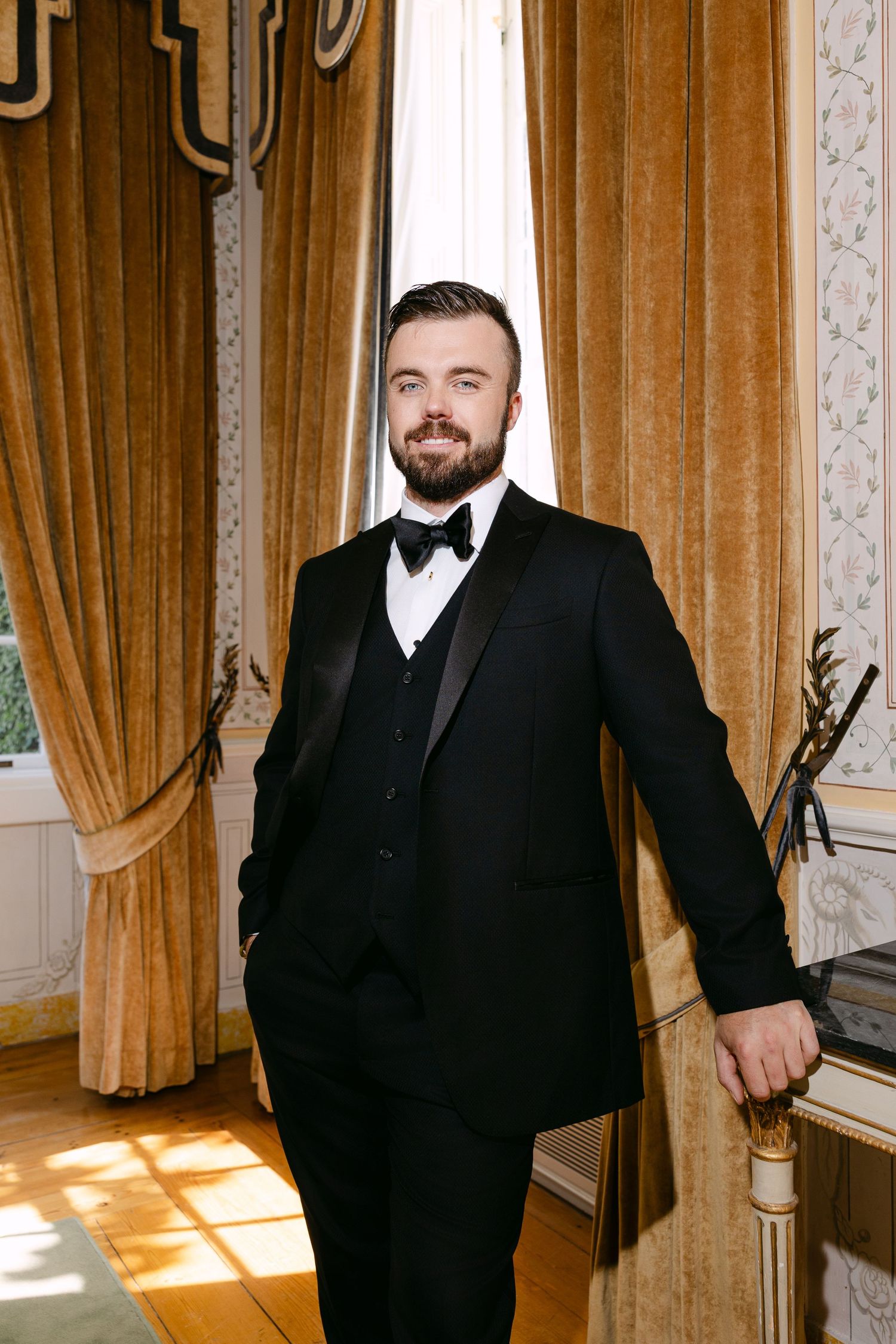 Formal portraits in elegant room with golden curtains and natural lighting.