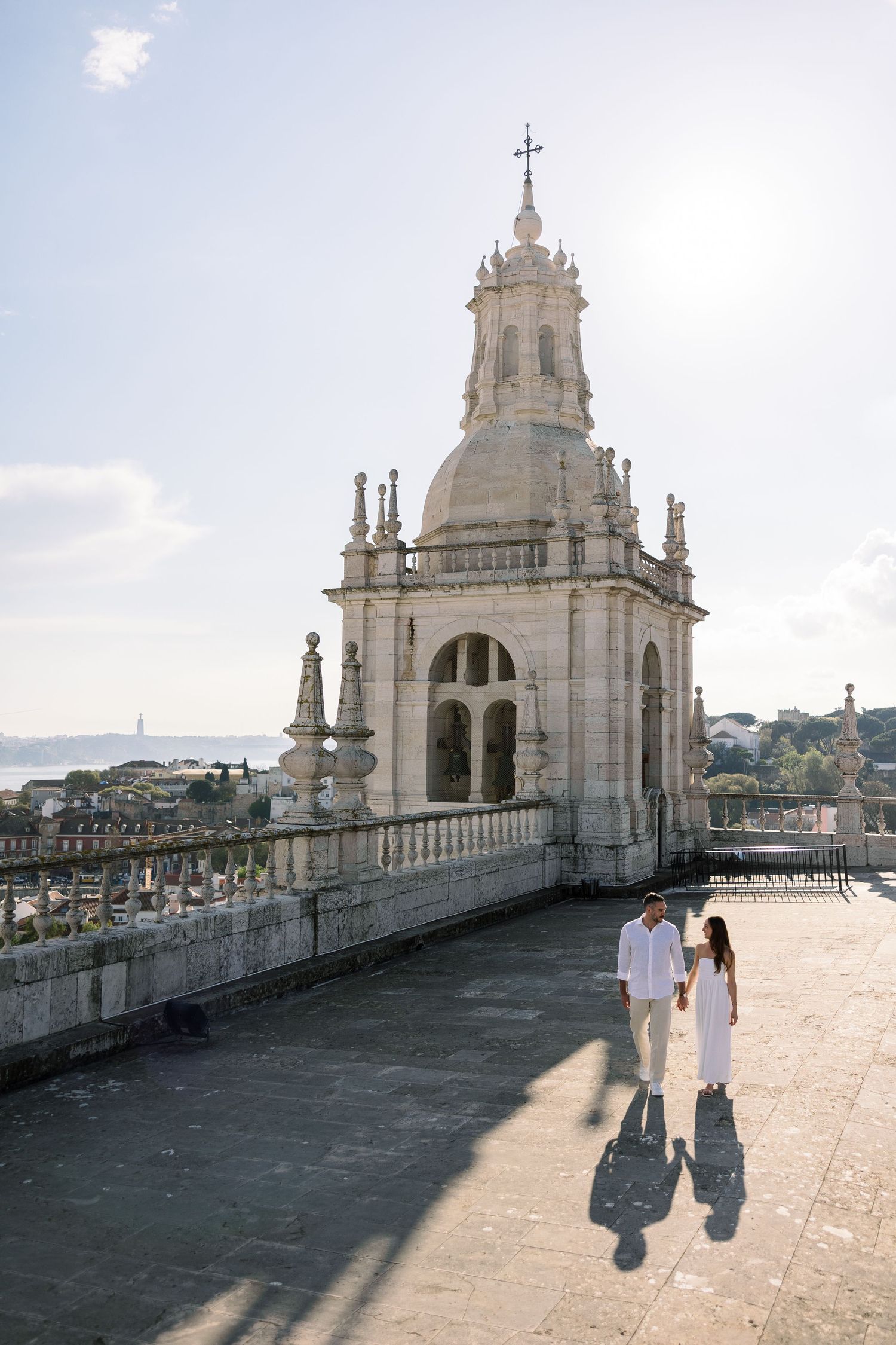 Couple holding hands on a sunlit rooftop terrace of a historic Portuguese cathedral with river views.