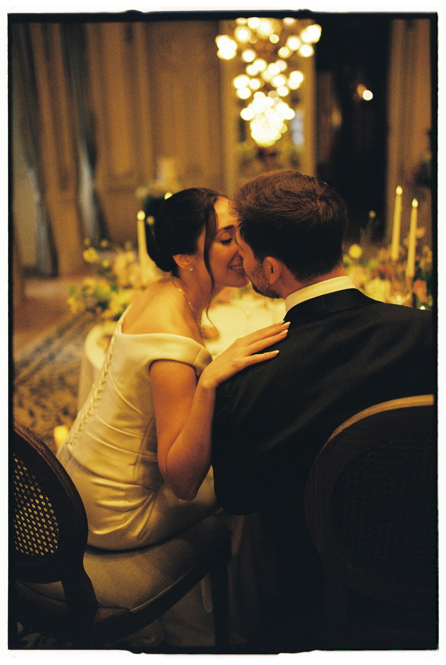 Bride and groom sharing a romantic kiss at their elegant candlelit wedding reception dinner table.