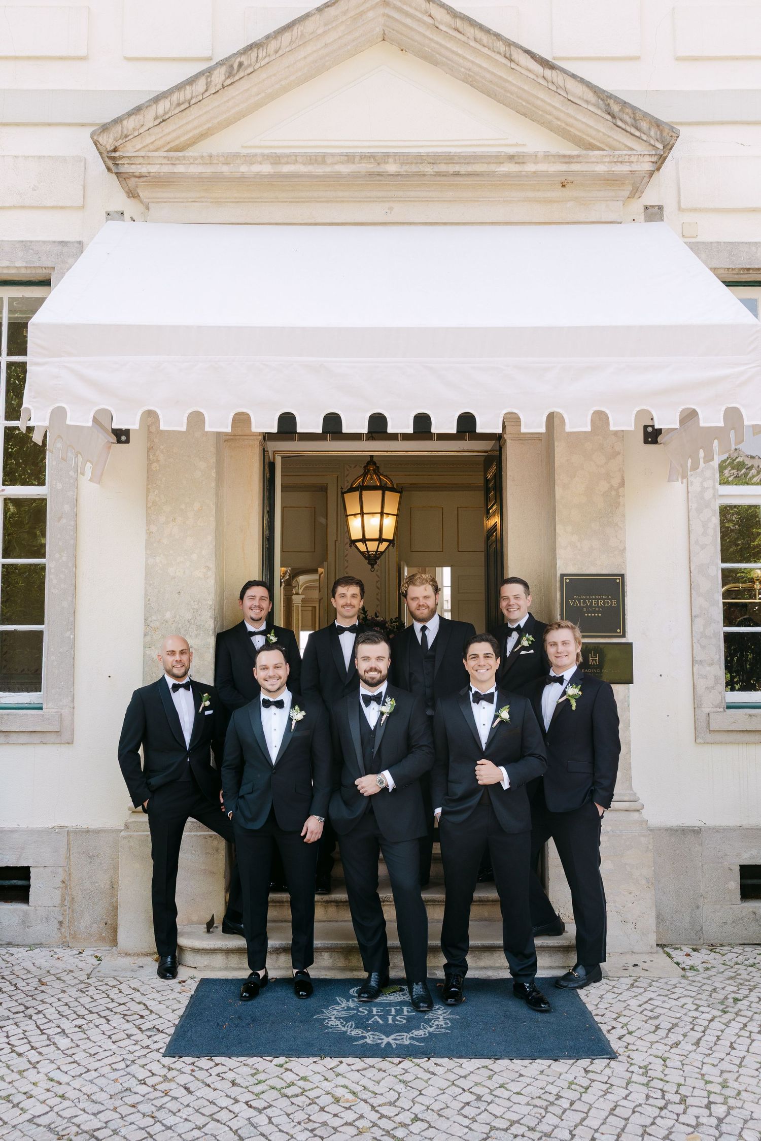 Wedding party in formal attire posed outside an elegant white building entrance.