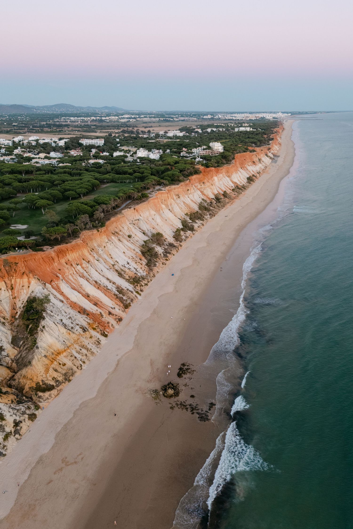 Aerial view of a dramatic coastline with orange cliffs meeting turquoise waters.