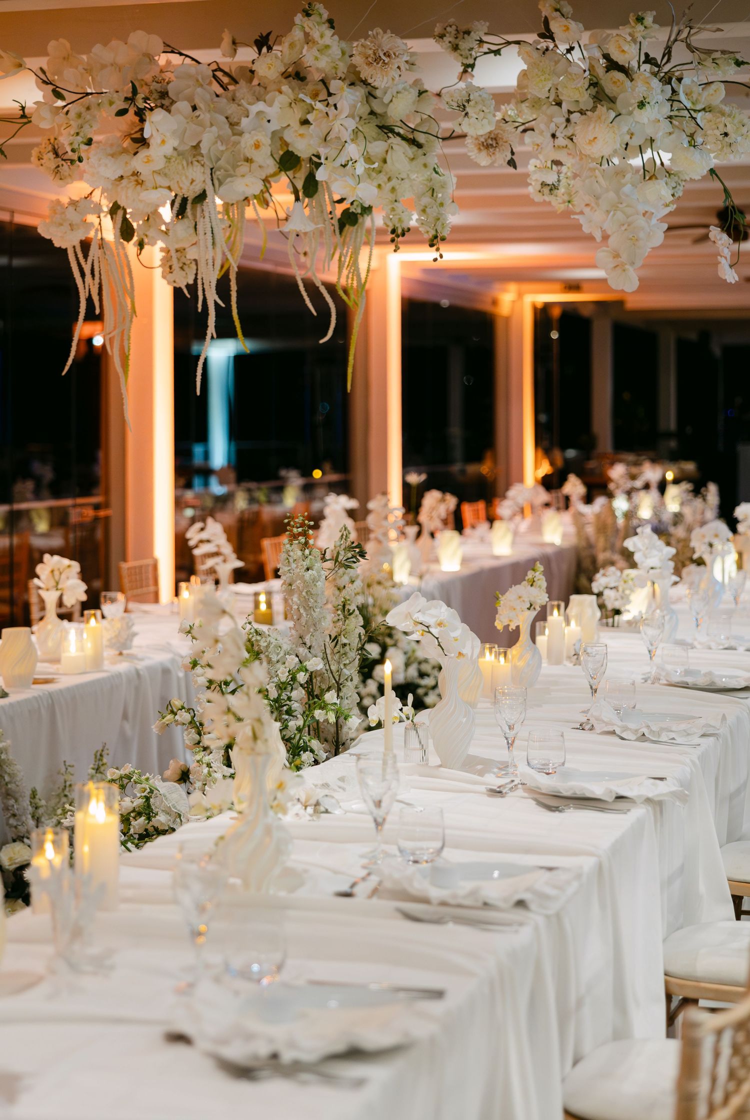 Luxurious wedding reception setup with white tablecloths and hanging floral arrangements in an elegant ballroom.