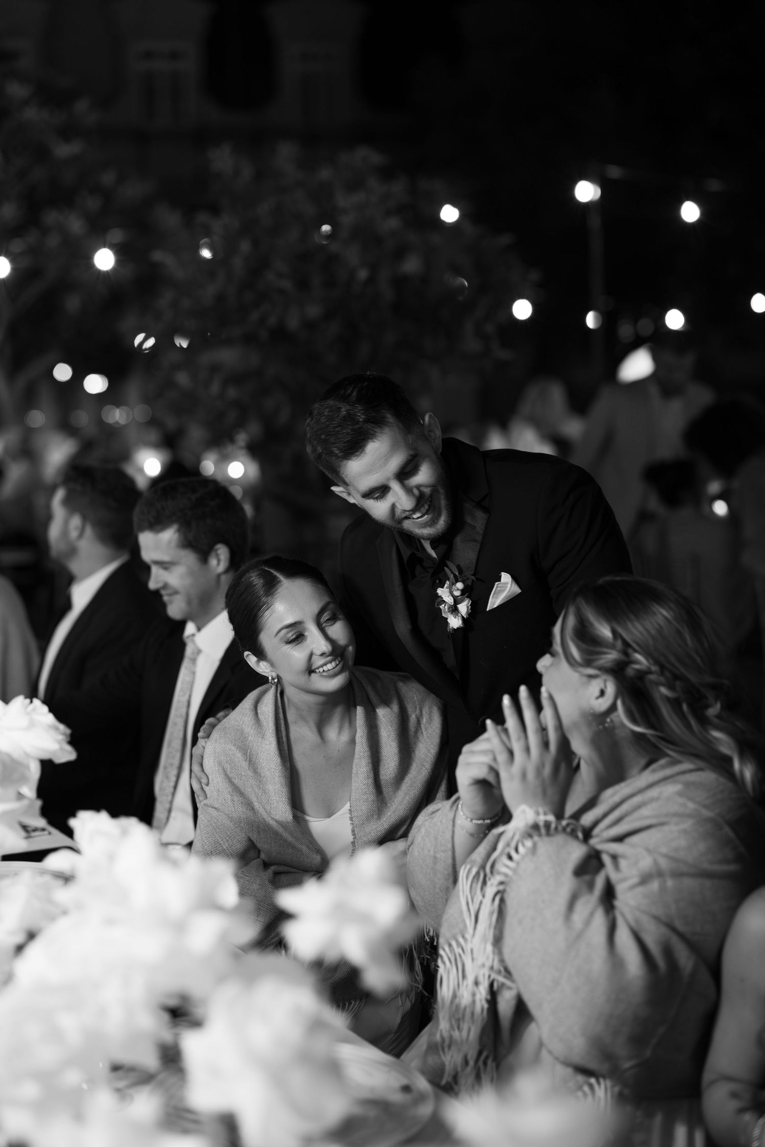 Wedding guests enjoying a lively celebration with string lights overhead at night.