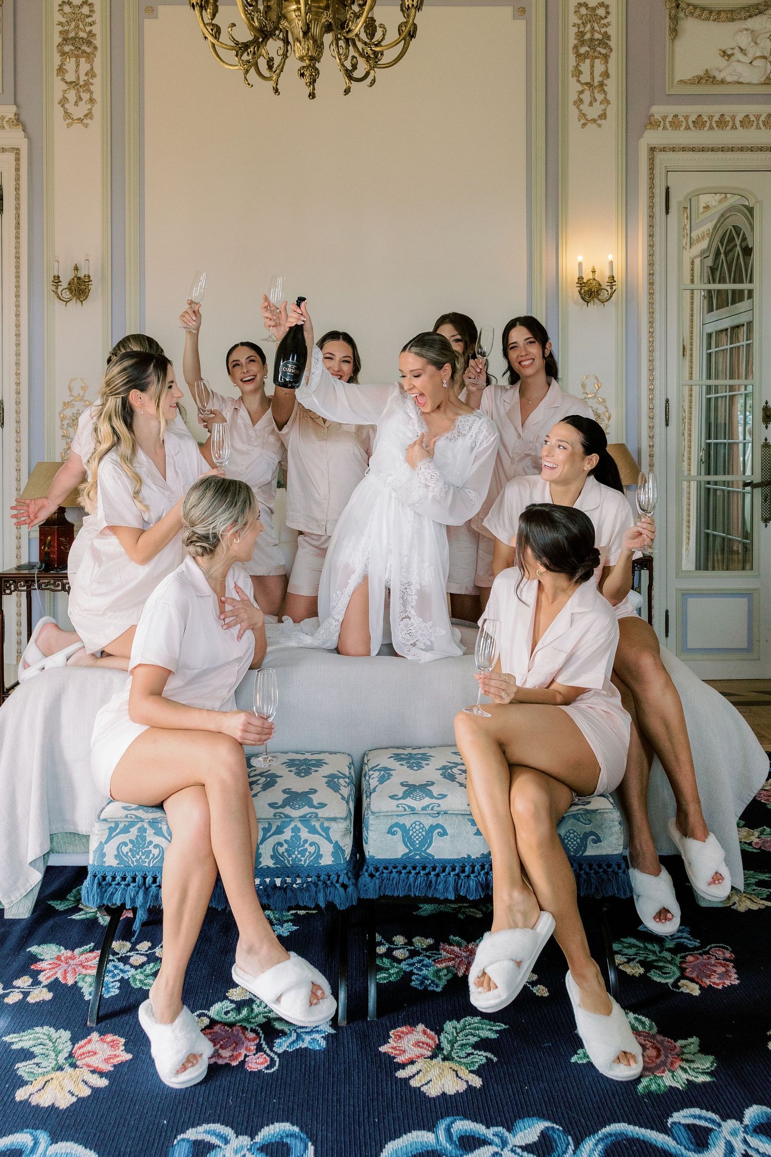 Group of bridesmaids in white robes celebrating on an elegant blue floral couch.