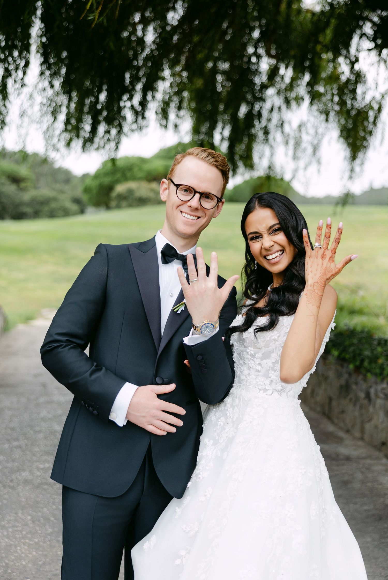 Happy newlyweds showing off their wedding rings with joyful smiles on a garden path.