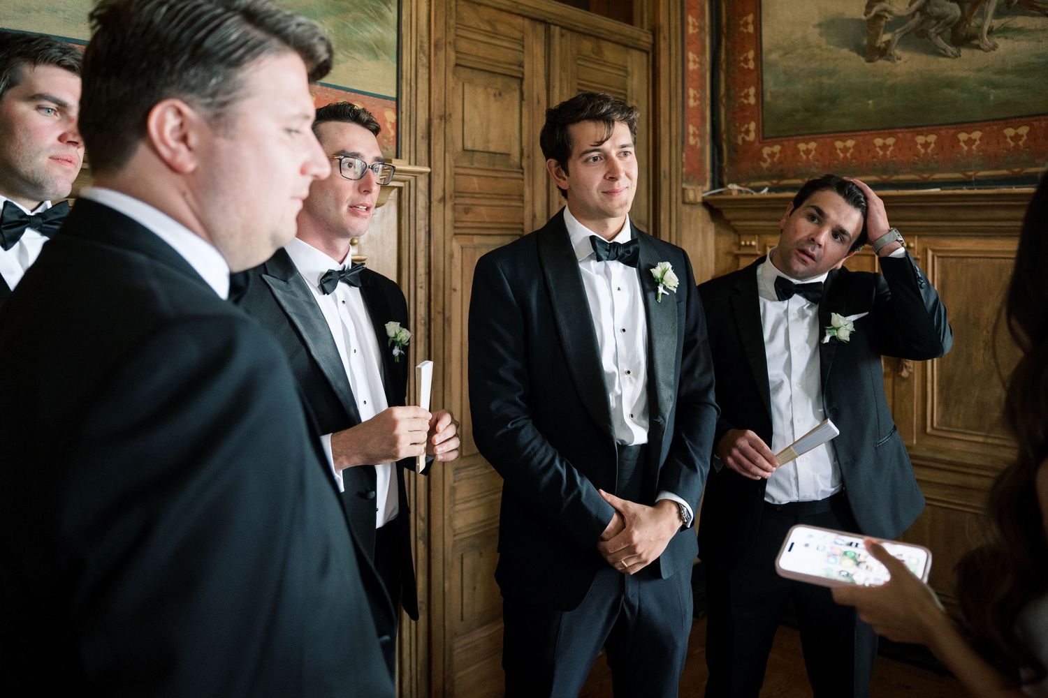 Groomsmen in black tuxedos share candid moments before the wedding ceremony.
