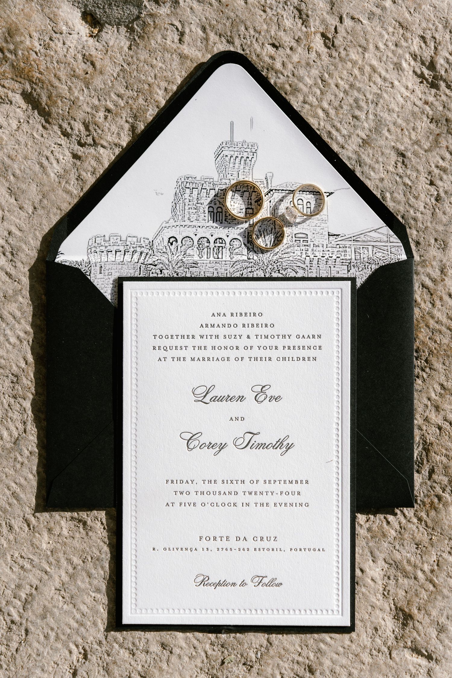 Wedding invitations with architectural sketch detail and black envelopes on stone surface.