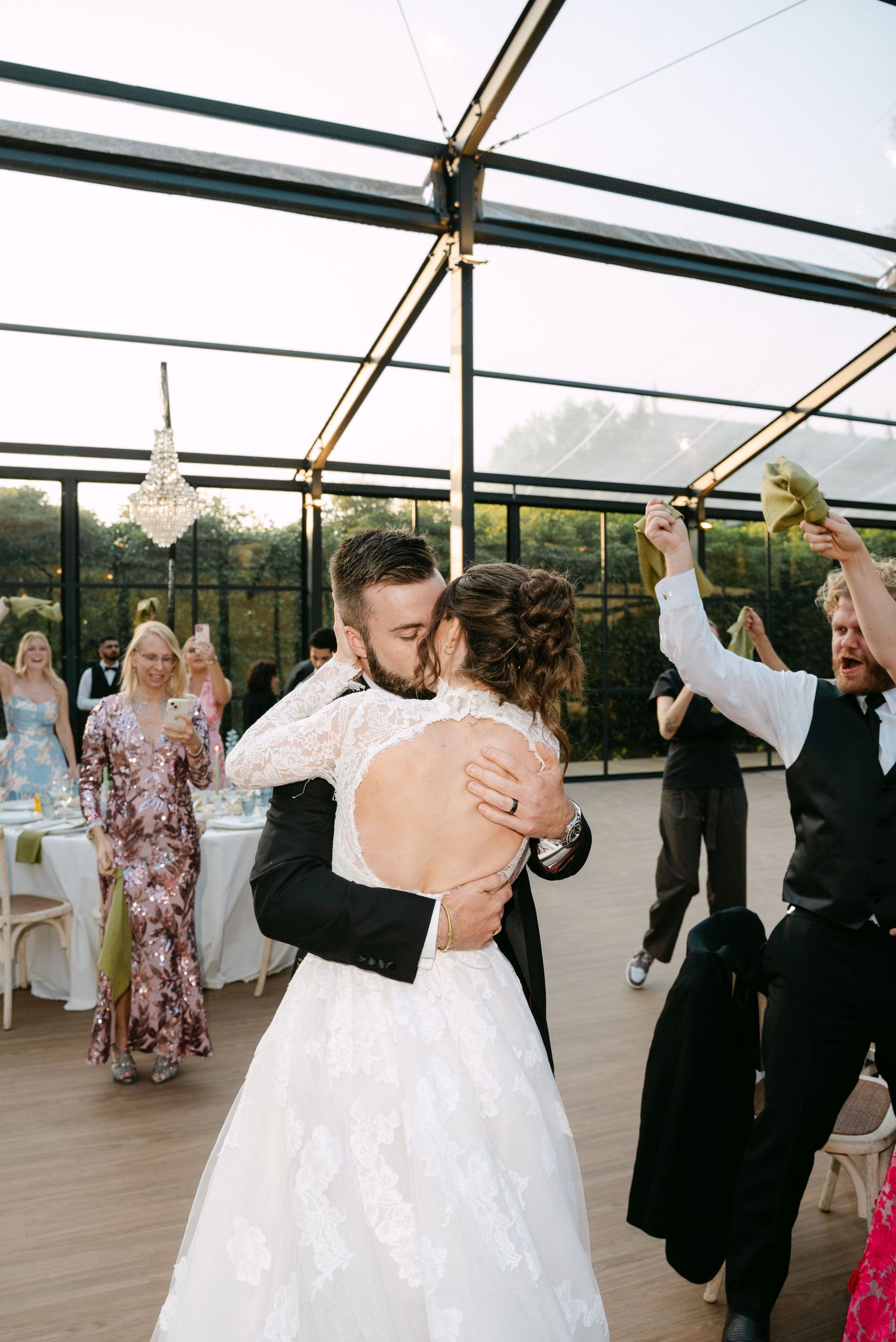 Wedding party dancing and celebrating under a glass ceiling venue.