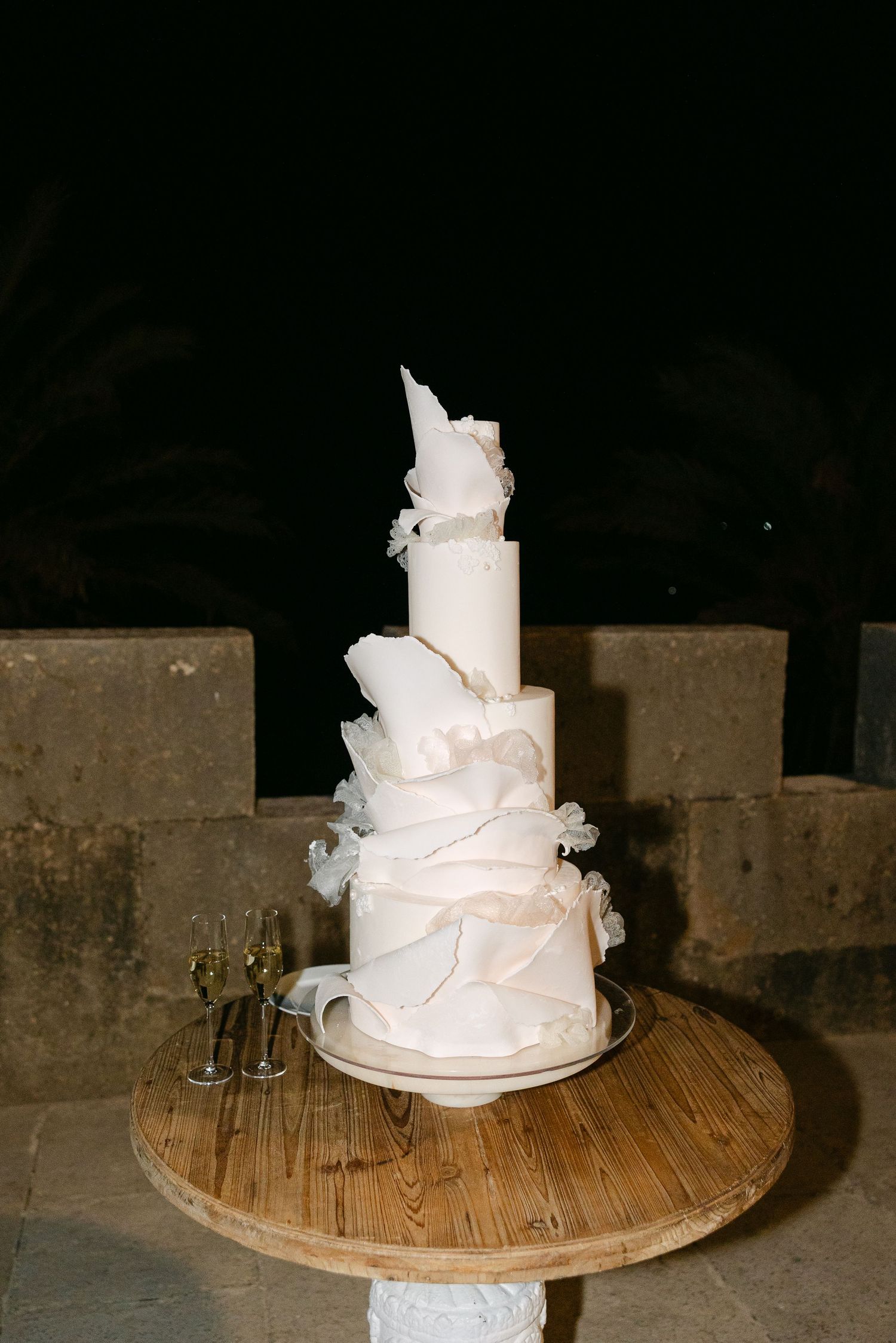 Modern white wedding cake with abstract sculptural details displayed on wooden table.