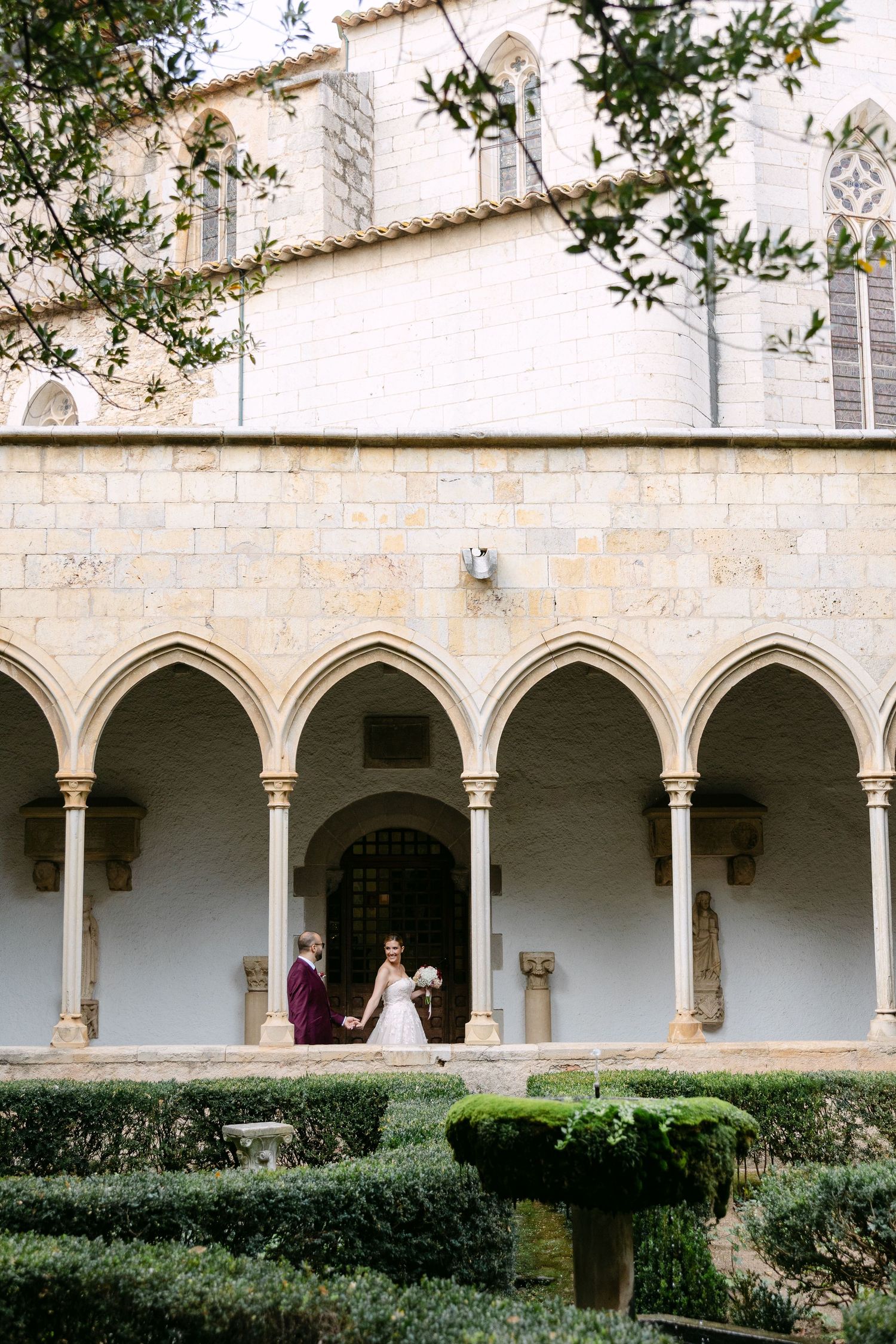 Historic monastery courtyard with Gothic arches provides stunning backdrop for wedding photos.