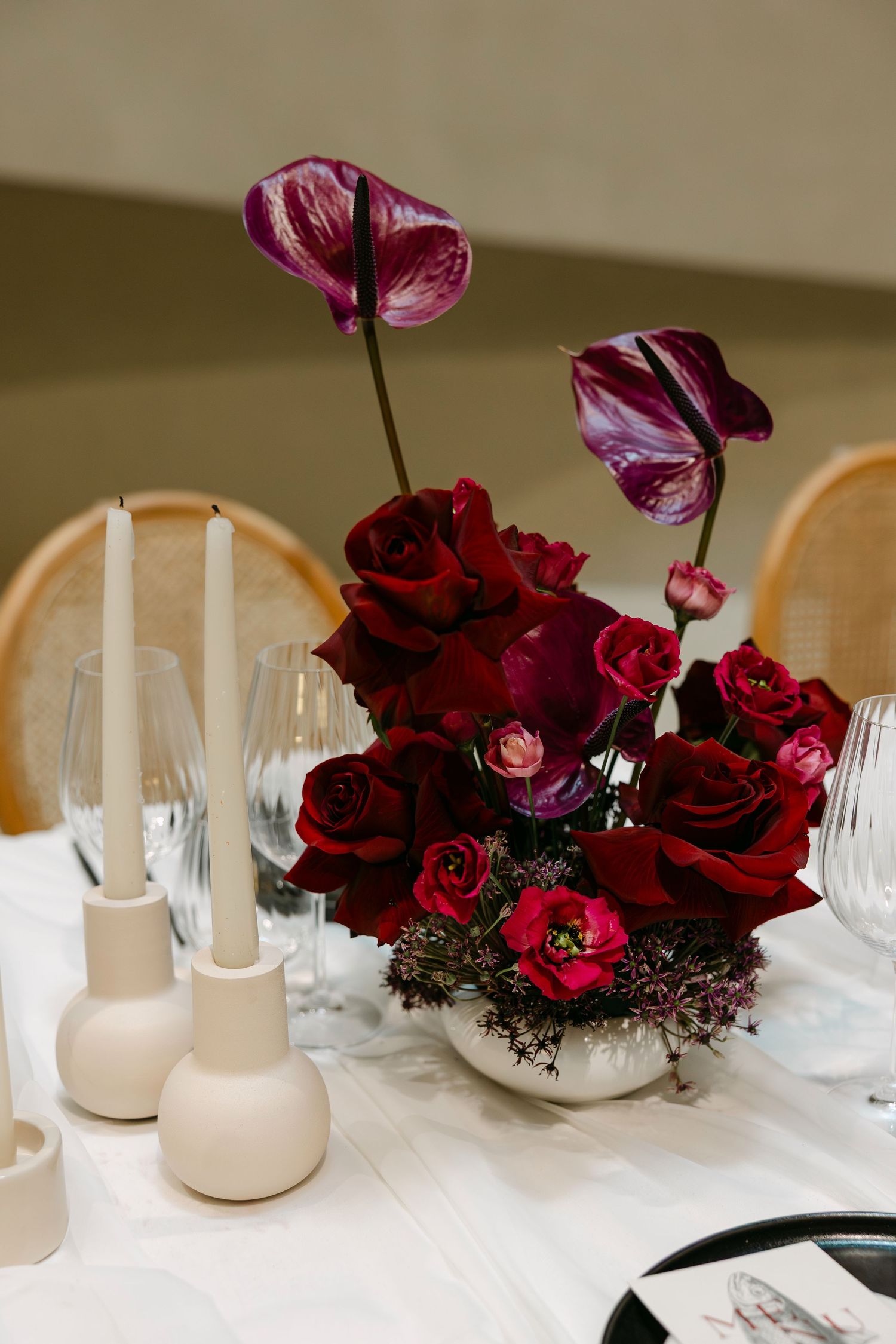 Deep burgundy roses and orchids arranged in modern centerpieces with white candle holders.
