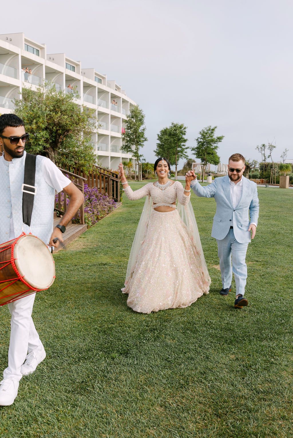 Wedding party members playfully posing on grassy hill outside venue.