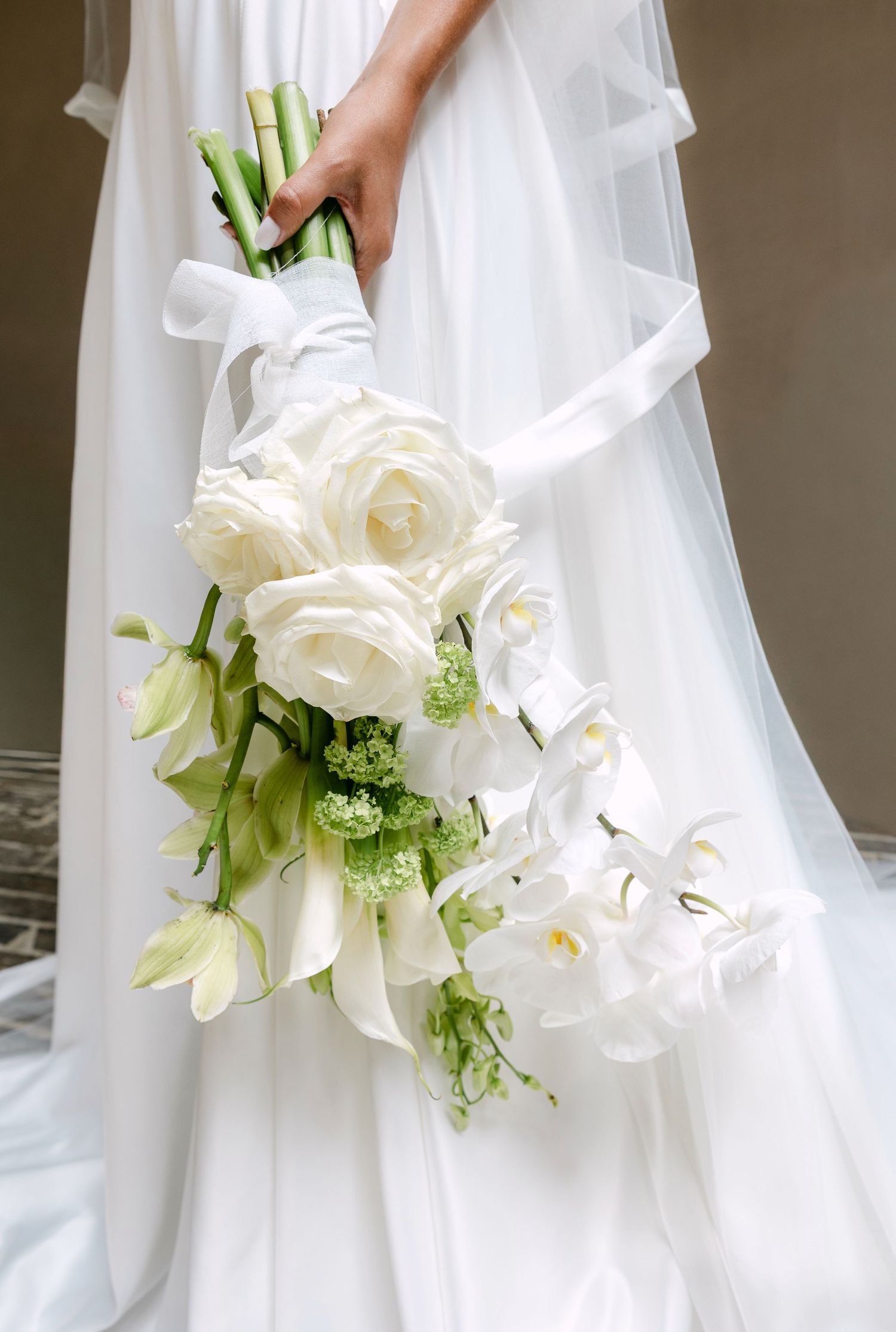 Elegant white wedding bouquet featuring roses, calla lilies and green accents against flowing white dress fabric.