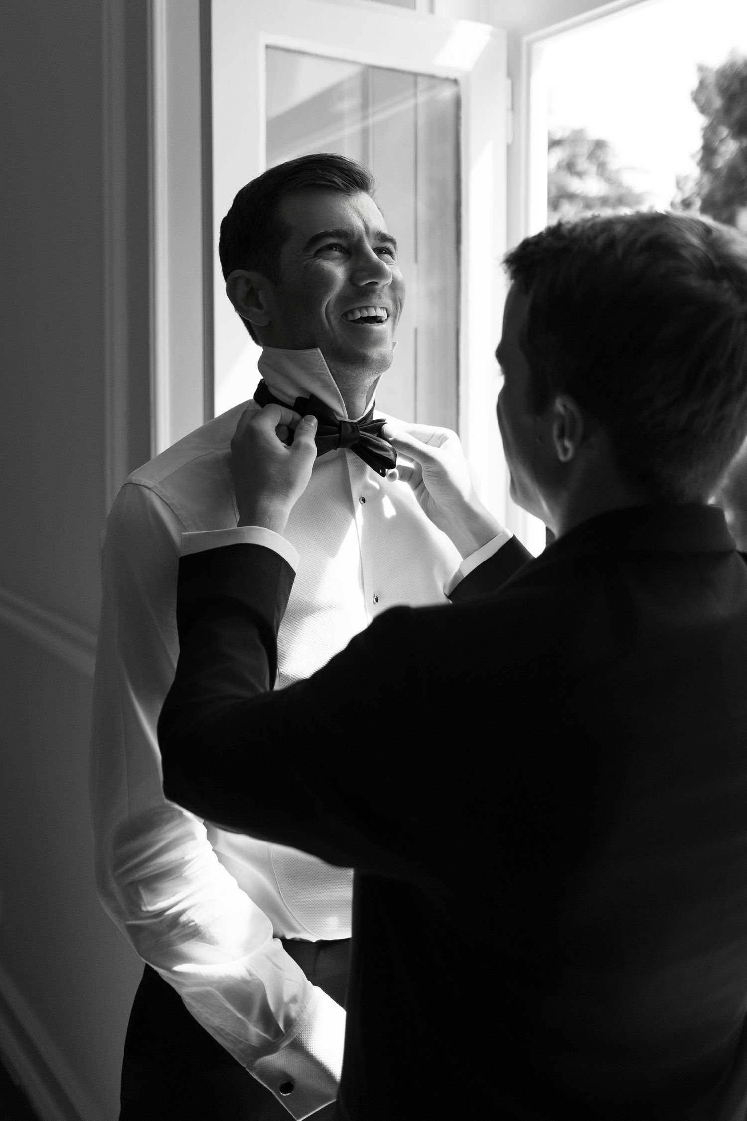 A candid black and white photo showing someone adjusting a bowtie in preparation for a formal event.
