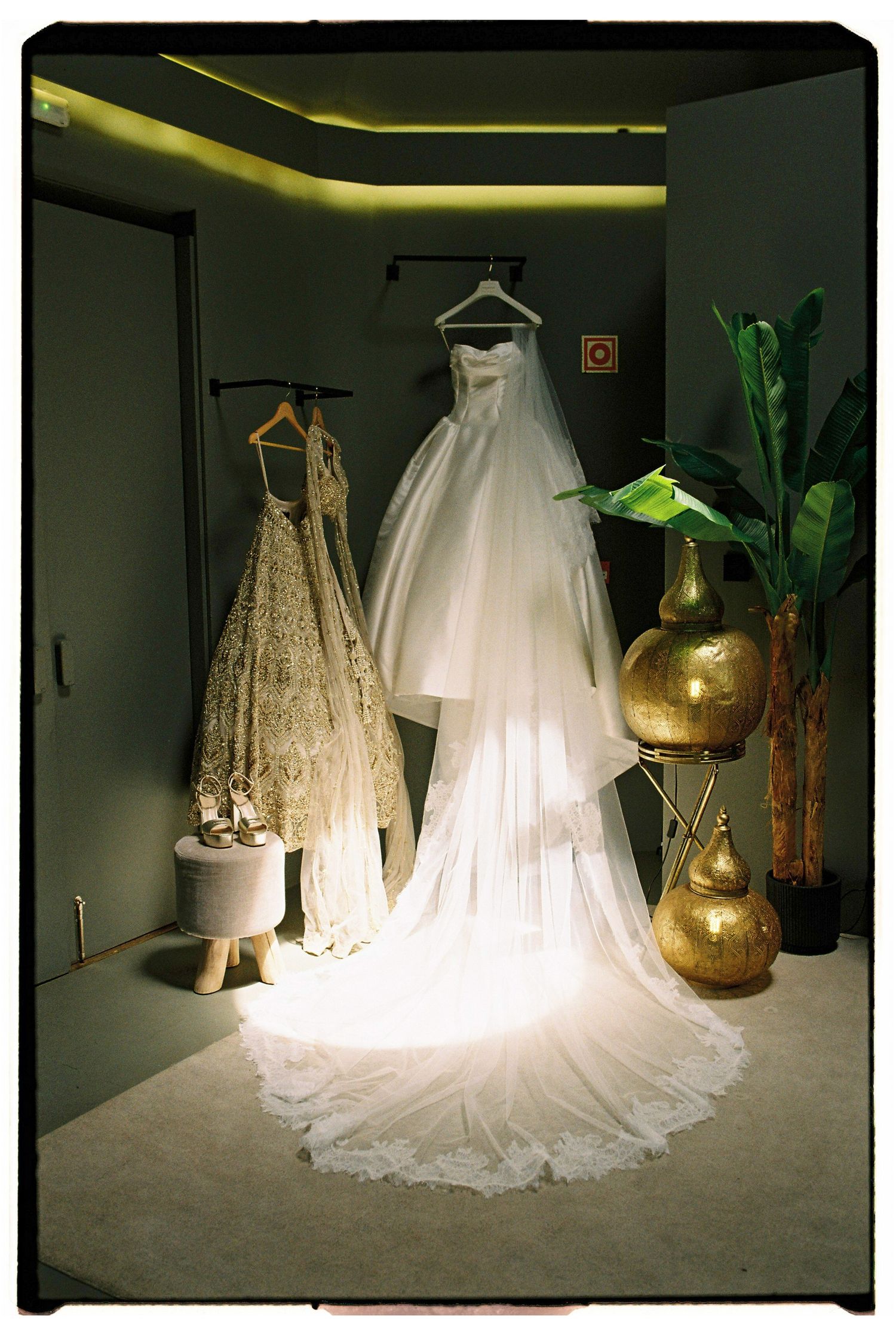Elegant bridal gown and bridesmaid dresses displayed in softly lit dressing room.