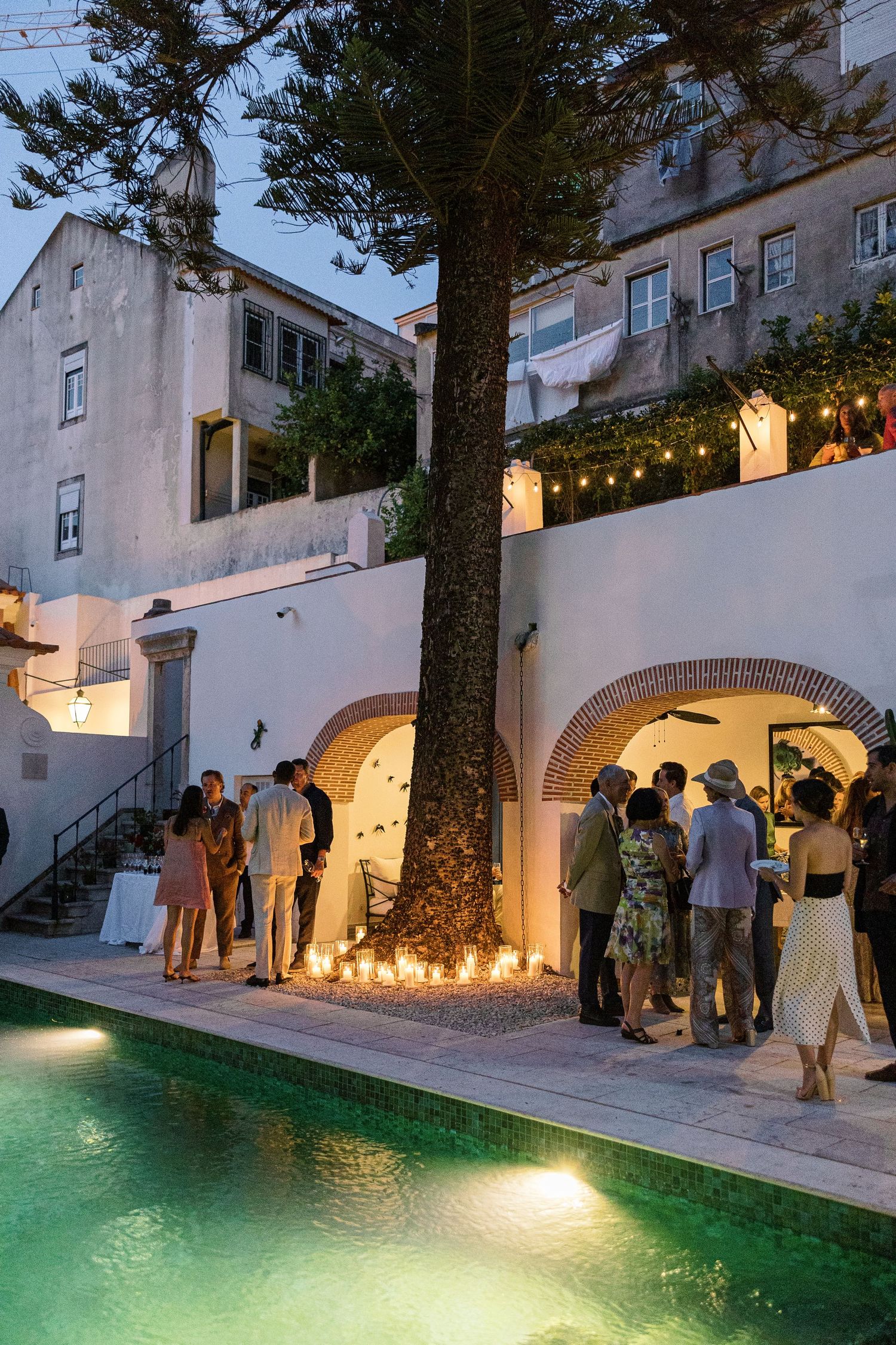 Elegant outdoor evening party by a pool with string lights, candles, and arched walls at a Mediterranean villa.